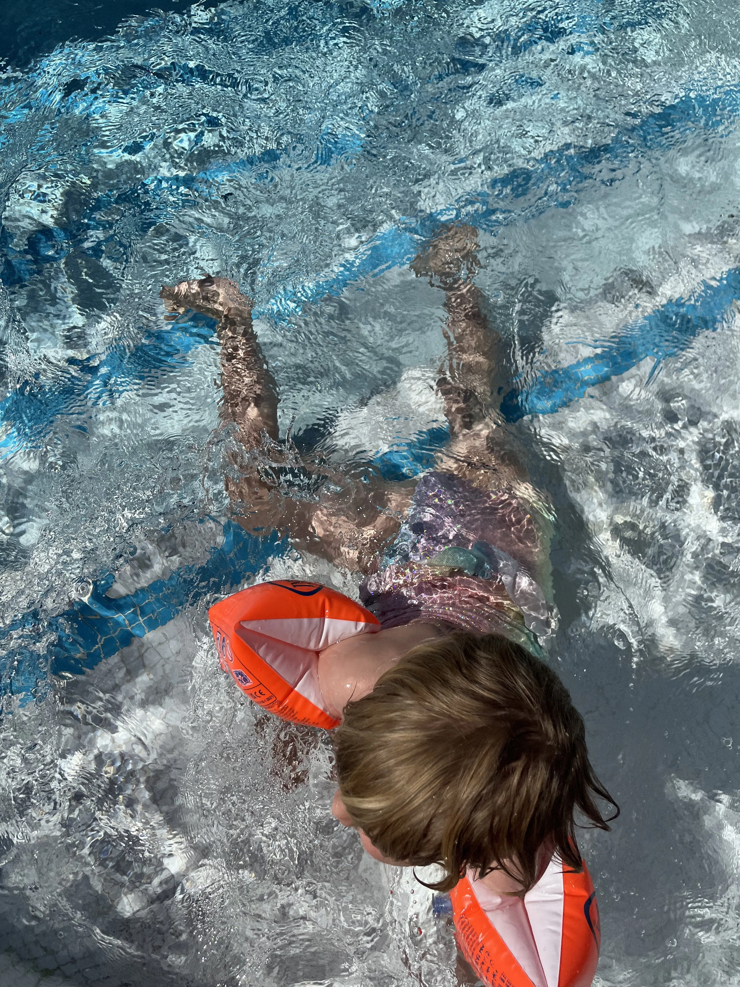 Child wearing an orange life jacket swimming in clear, rippling blue water