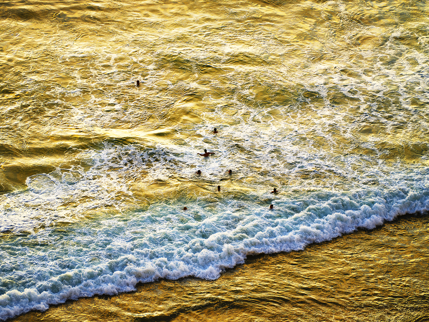Sunset over ocean with several people swimming and waves crashing onto shore.