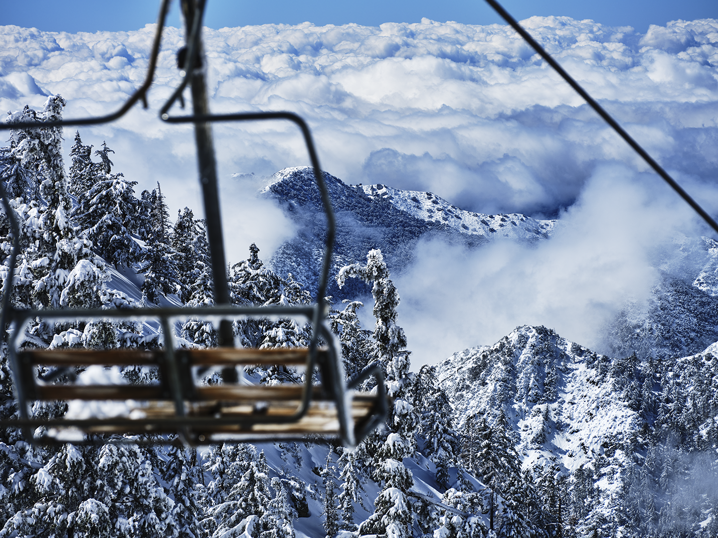 Snow-covered mountain landscape viewed from a ski lift, with snow-laden trees and a cloudy sky.