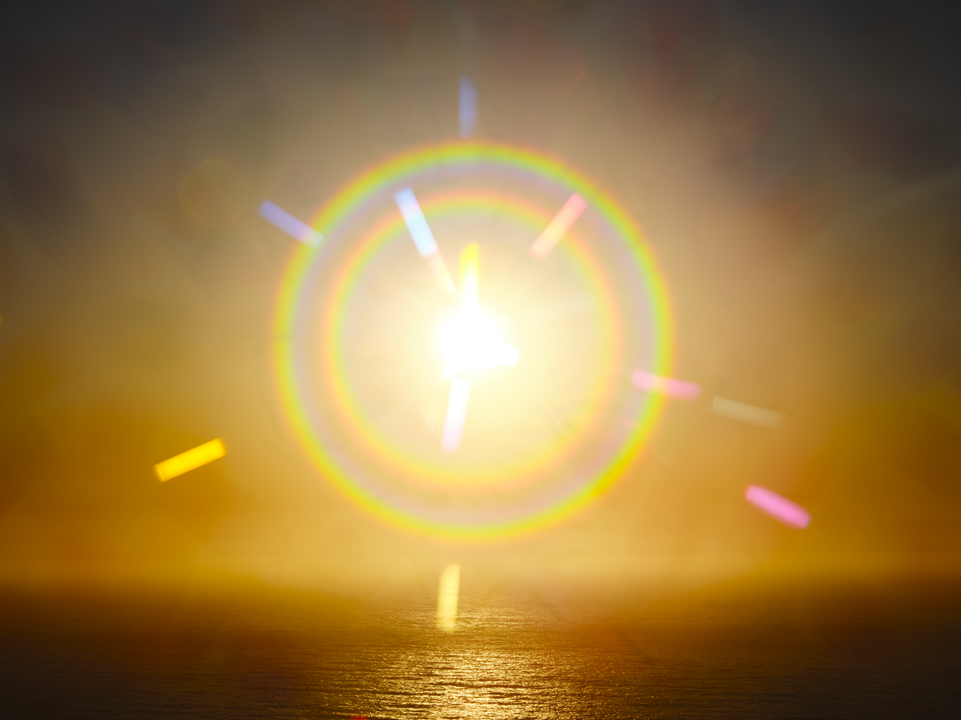 Sunset over the ocean with a bright glow and rainbow lens flare.