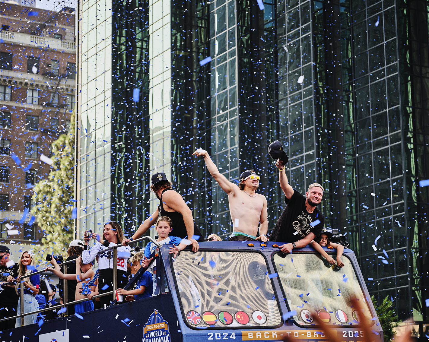 People celebrating on a parade float during a city parade with confetti and a modern glass building in the background.