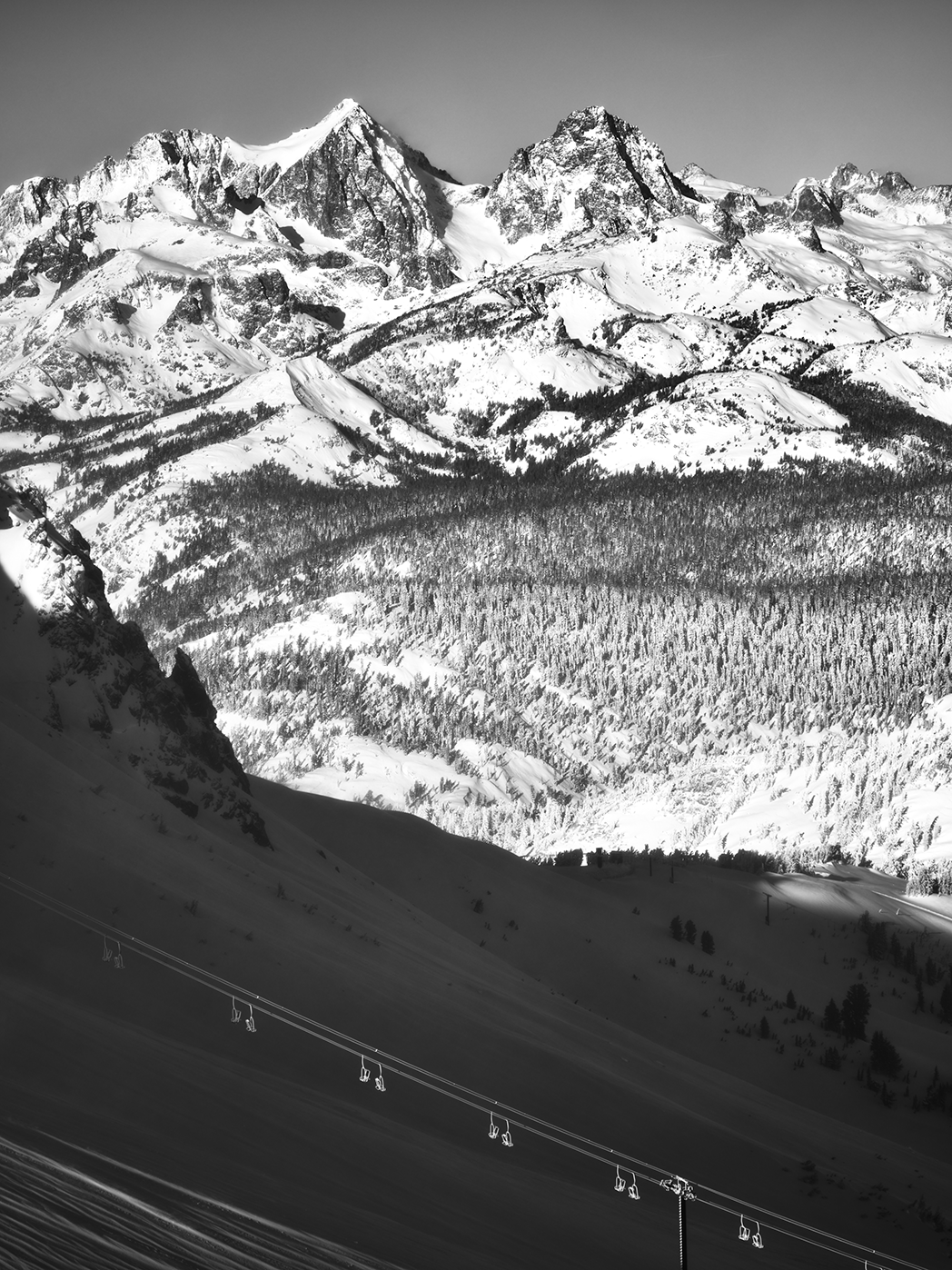 Snow-covered mountain range with ski lift chairs in the foreground, black and white photo.