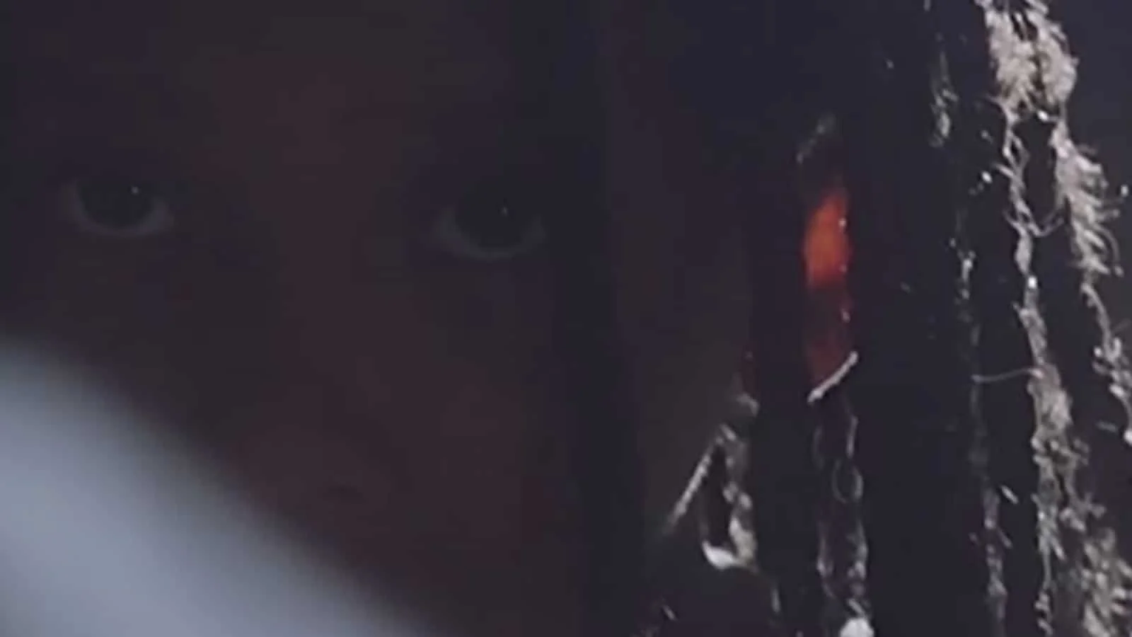 A close-up of a person's face partially obscured by darkness with visible eyes and some hair.