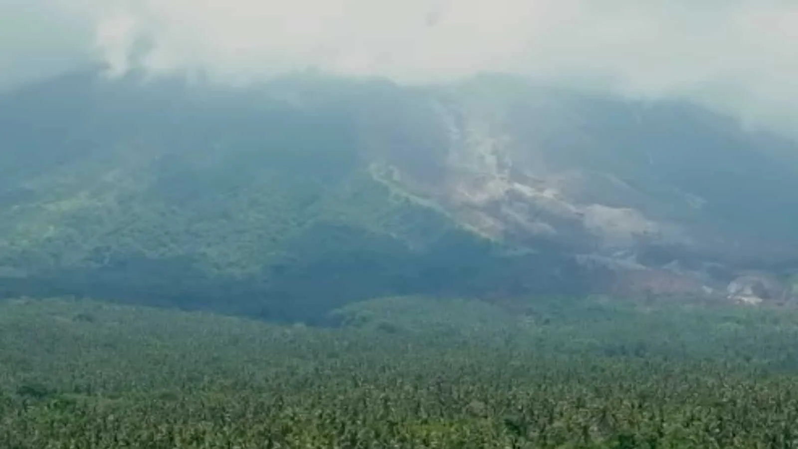 A hilly landscape with volcano damaged forests and smoke-covered mountains.