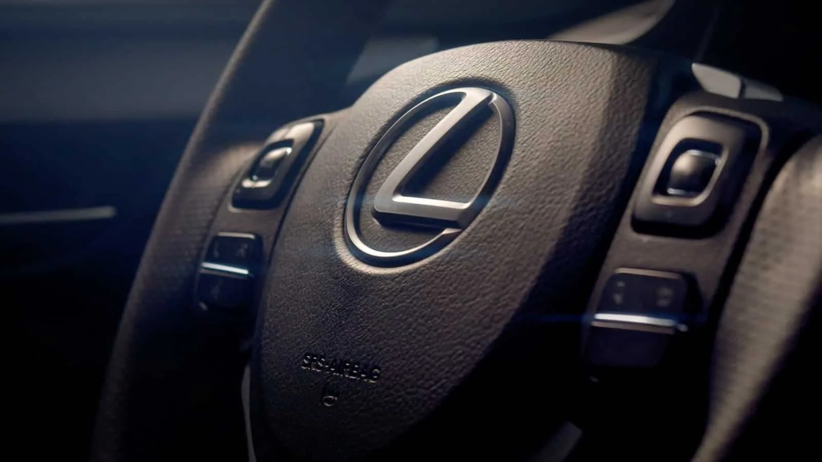 Close-up of a Lexus steering wheel with control buttons and the Lexus logo in the center.