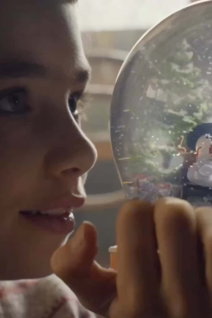 A young child peering through a snow globe, with a clear view of the winter scene inside.
