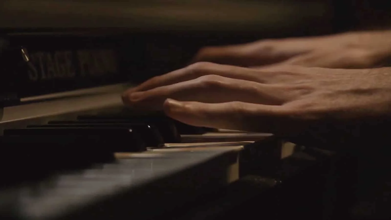 Close-up of hands playing piano keys in a dark setting.