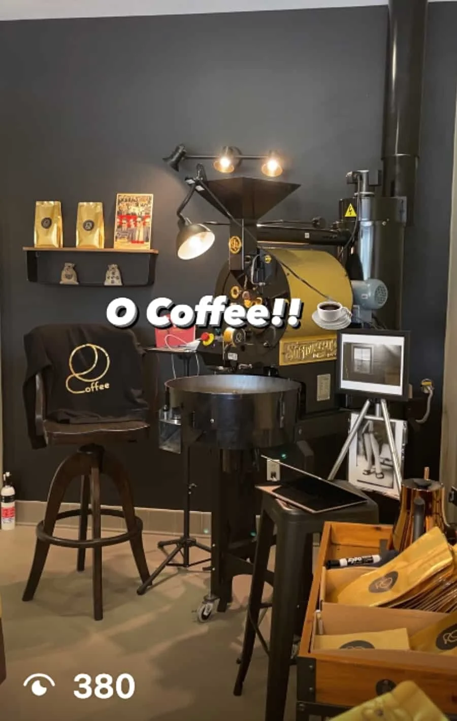 A coffee roasting machine in a coffee shop with shelves, cups, a framed photo, and packets of coffee beans around it.