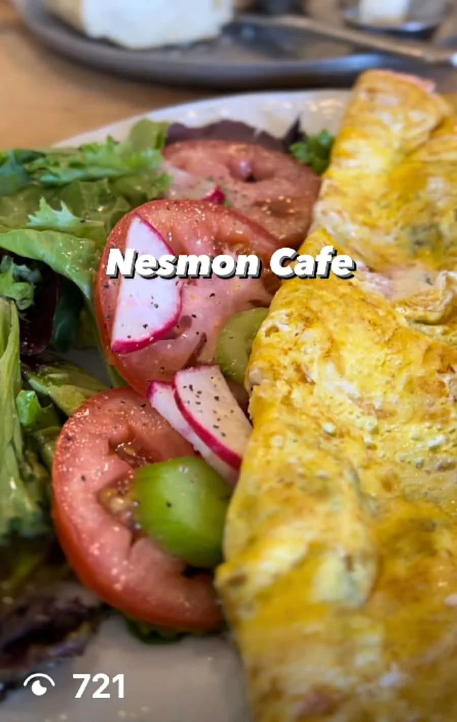 Close-up of a plate with a salad containing lettuce, sliced radishes, and cherry tomatoes, and an omelette at Nesmon Cafe.
