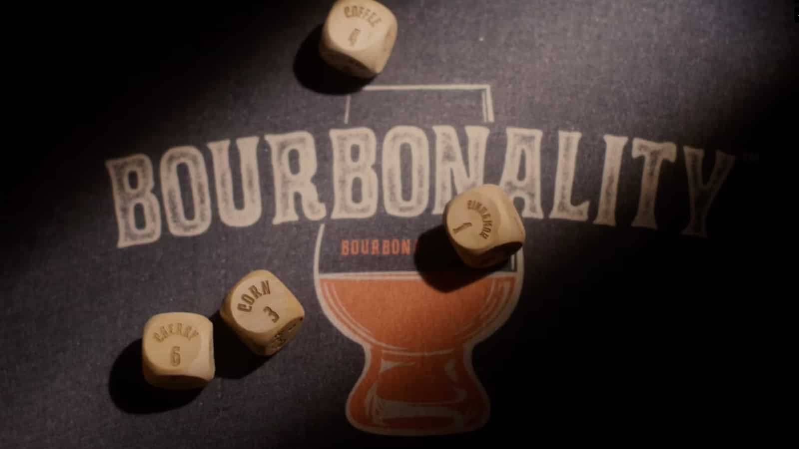 Three beige dice with black and brown lettering, placed on a dark surface with a logo title "Bourbonality." The logo features a large glass filled with bourbon.