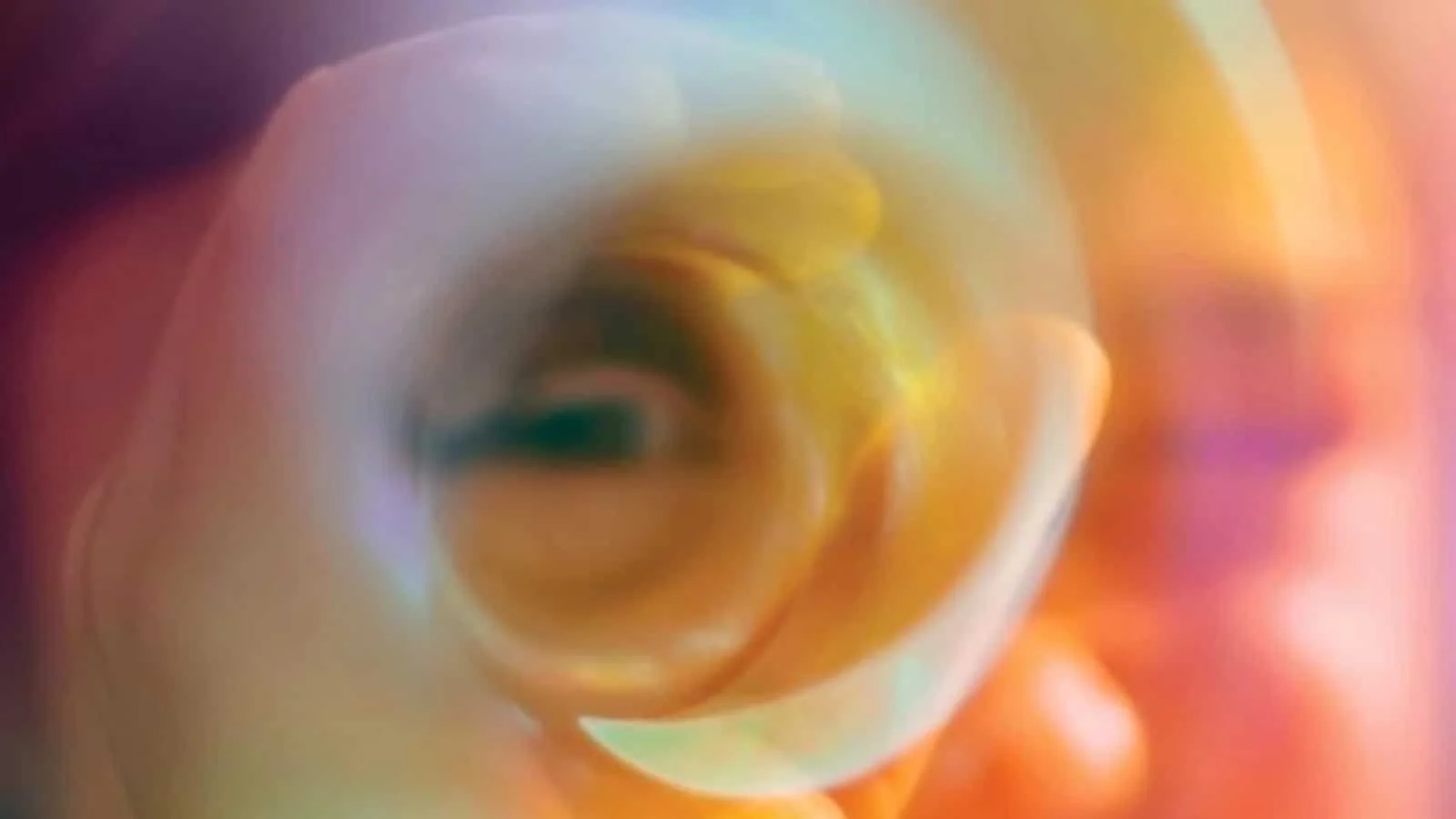Close-up view looking into the opening of a transparent tube or bottle, blurred, with vibrant colors and reflections.