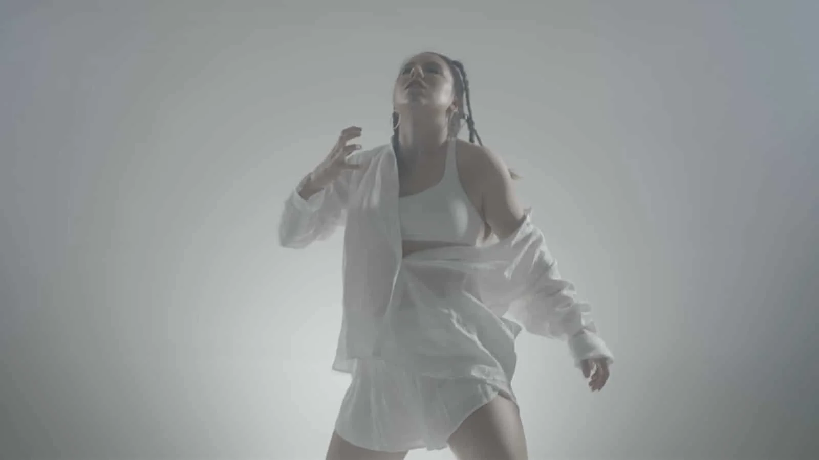 A woman dancing, dressed in a white outfit with a jacket, against a plain, light gray background.
