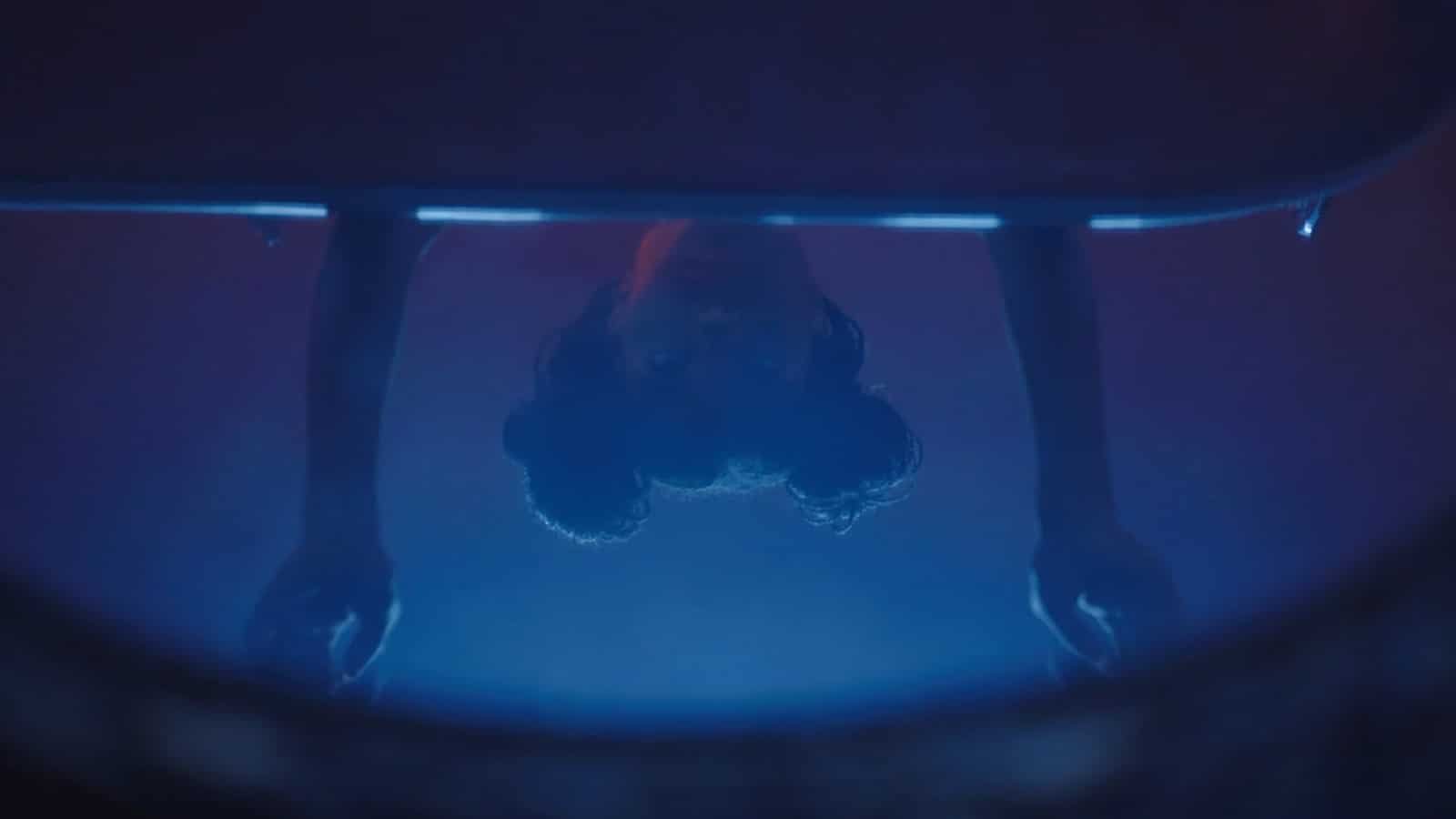 An individual is seen from below, in a dimly lit area with blue lighting.