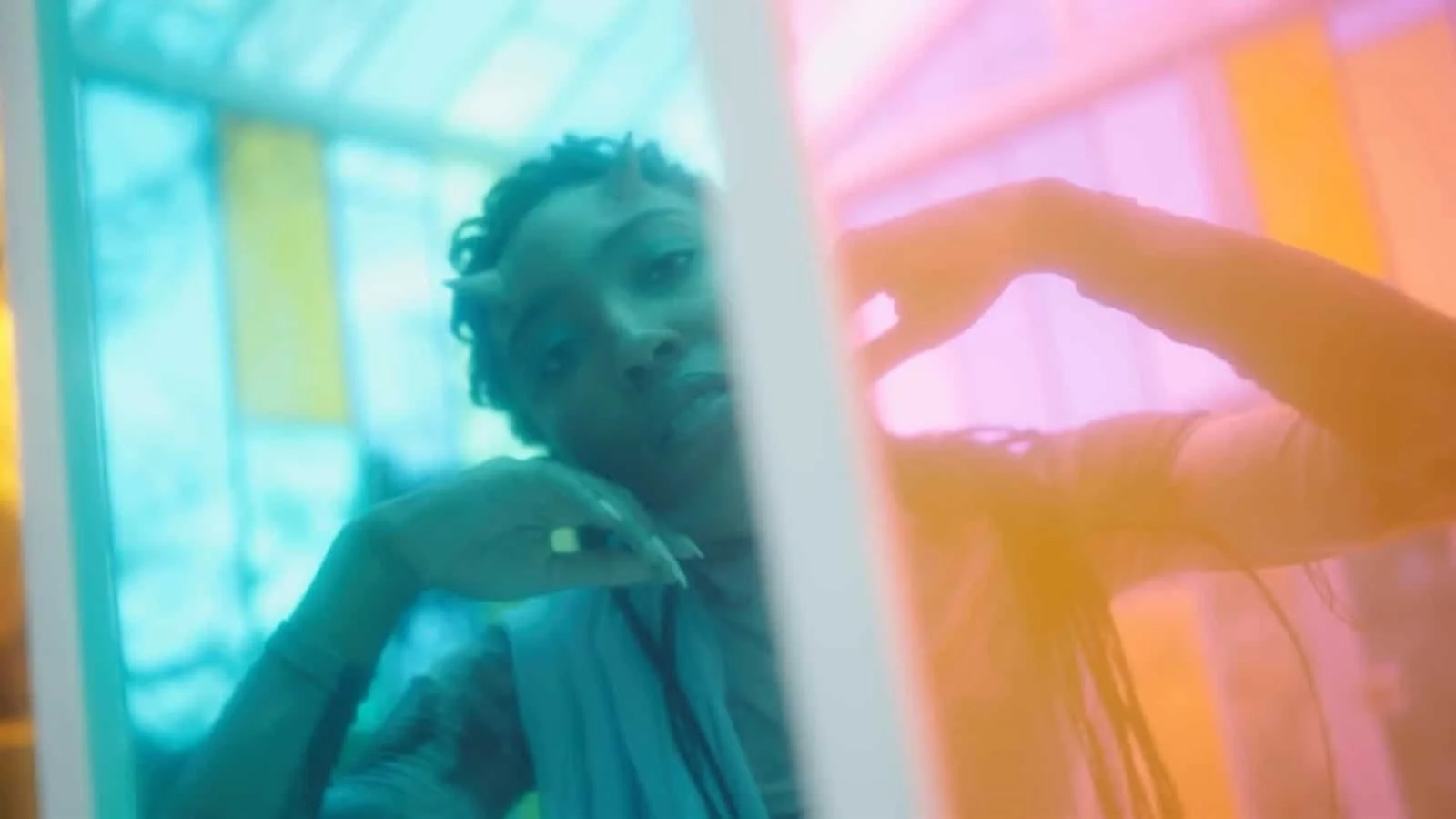 A young person looking into a colorful, vertically divided glass surface with blue, pink, and yellow lighting effects.