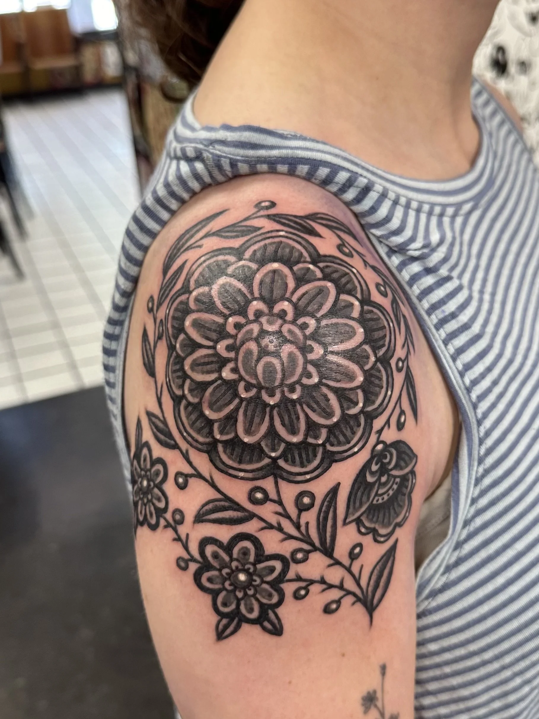 Black floral tattoo on person's upper arm featuring multiple flowers, leaves, and decorative elements.