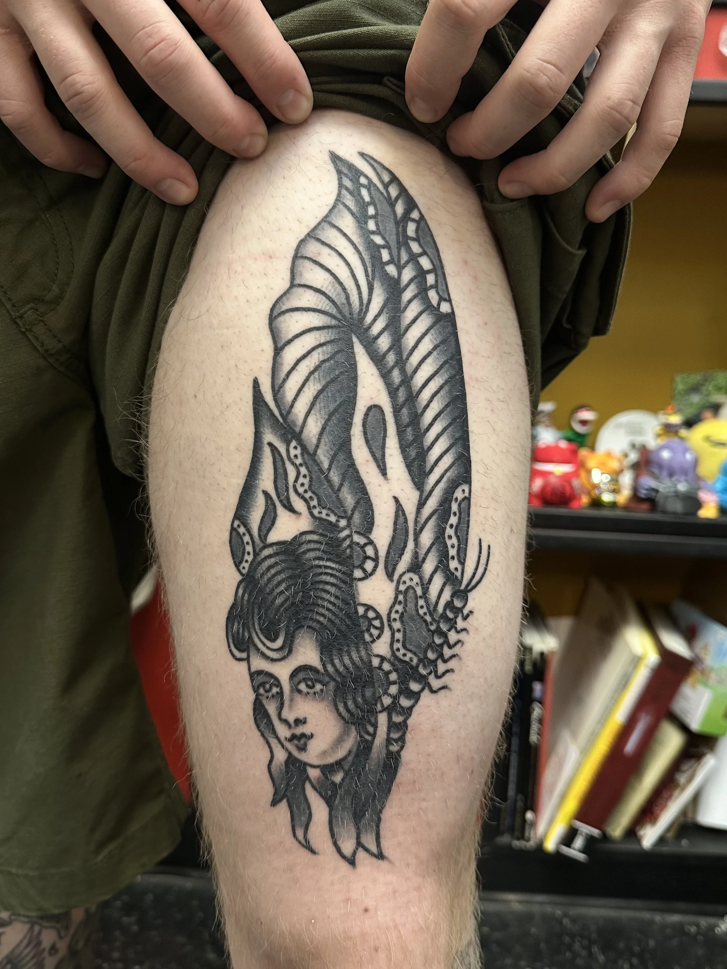 A black tattoo of a dragon on a person's upper arm, with detailed wings and a serpentine body, held by hands pulling the sleeve up.