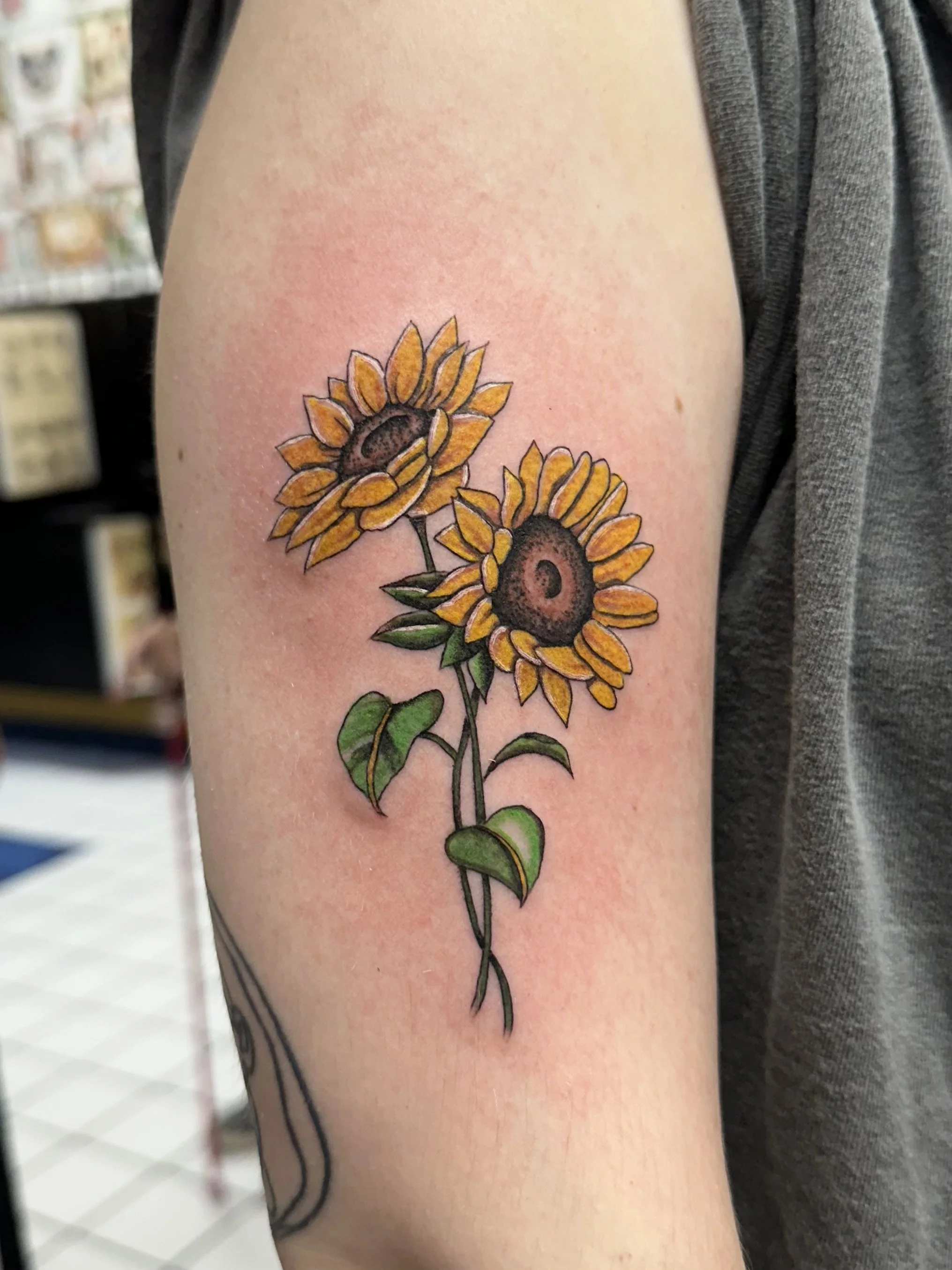 Tattoo of two sunflowers with green leaves on a person's upper arm.