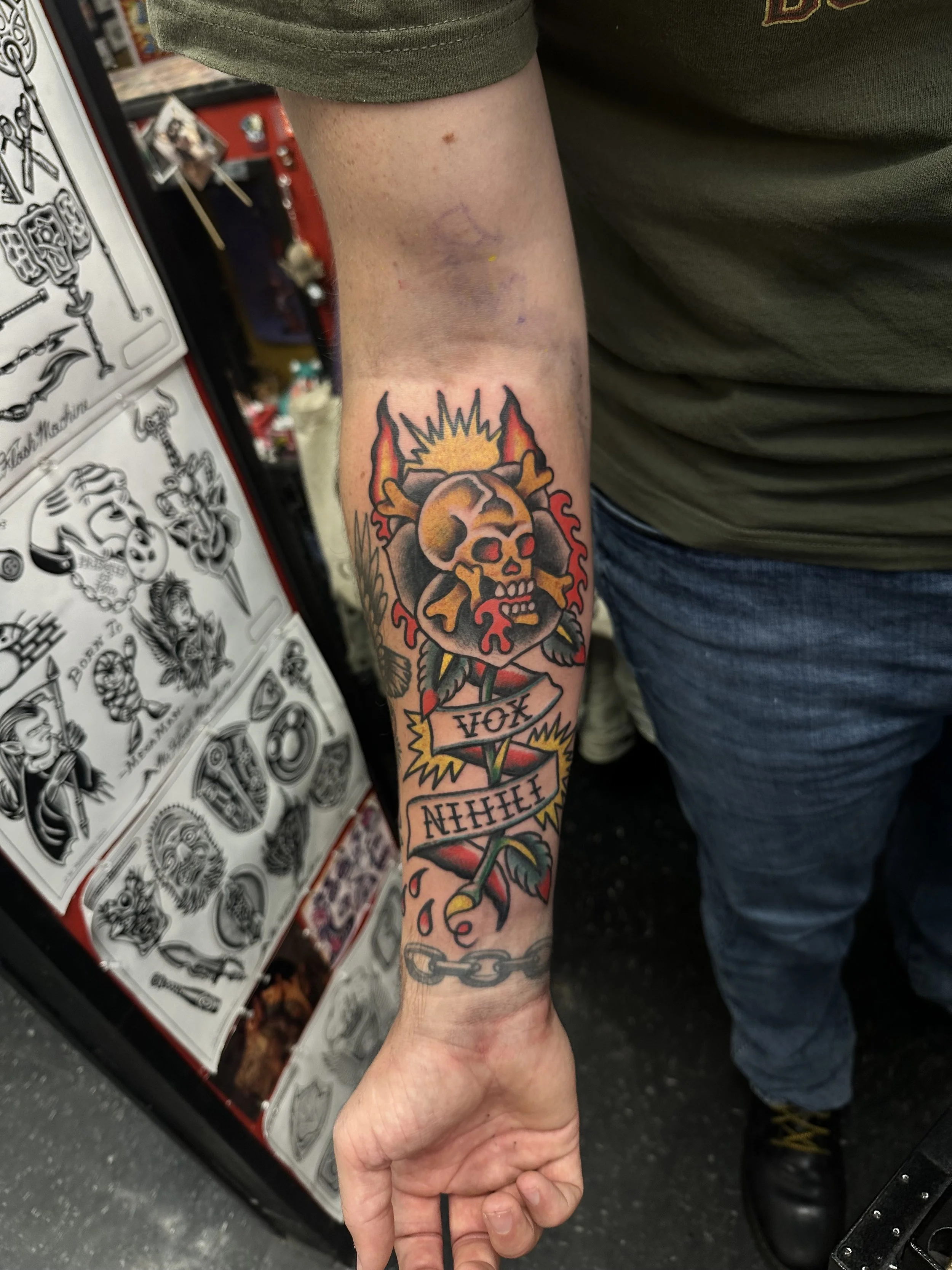 Tattoo of a skull with flames on the arm, featuring a banner reading 'IF OX' with additional text below.