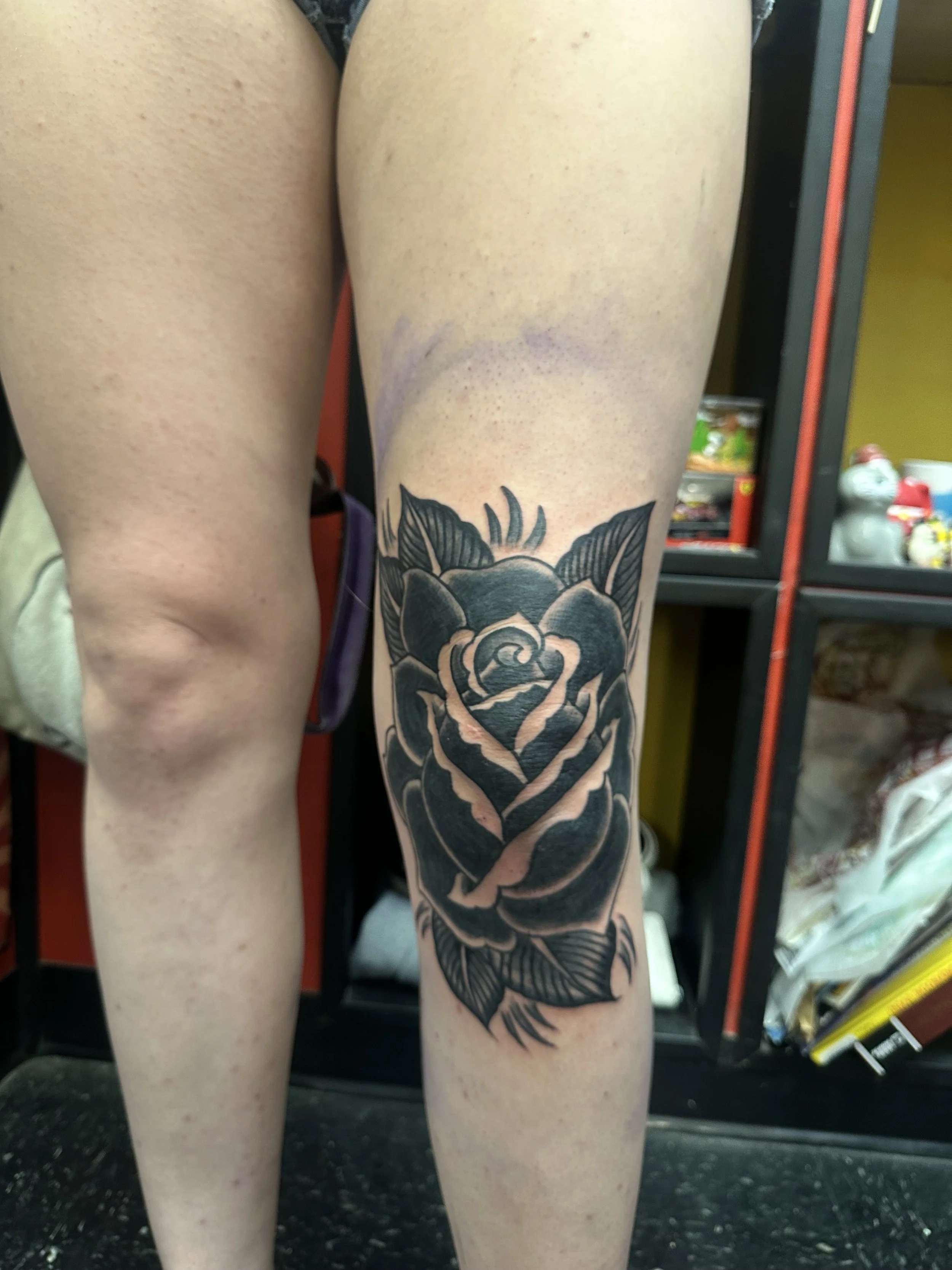 Close-up of a person's thigh with a large black and gray floral tattoo, set against a background of gym equipment.