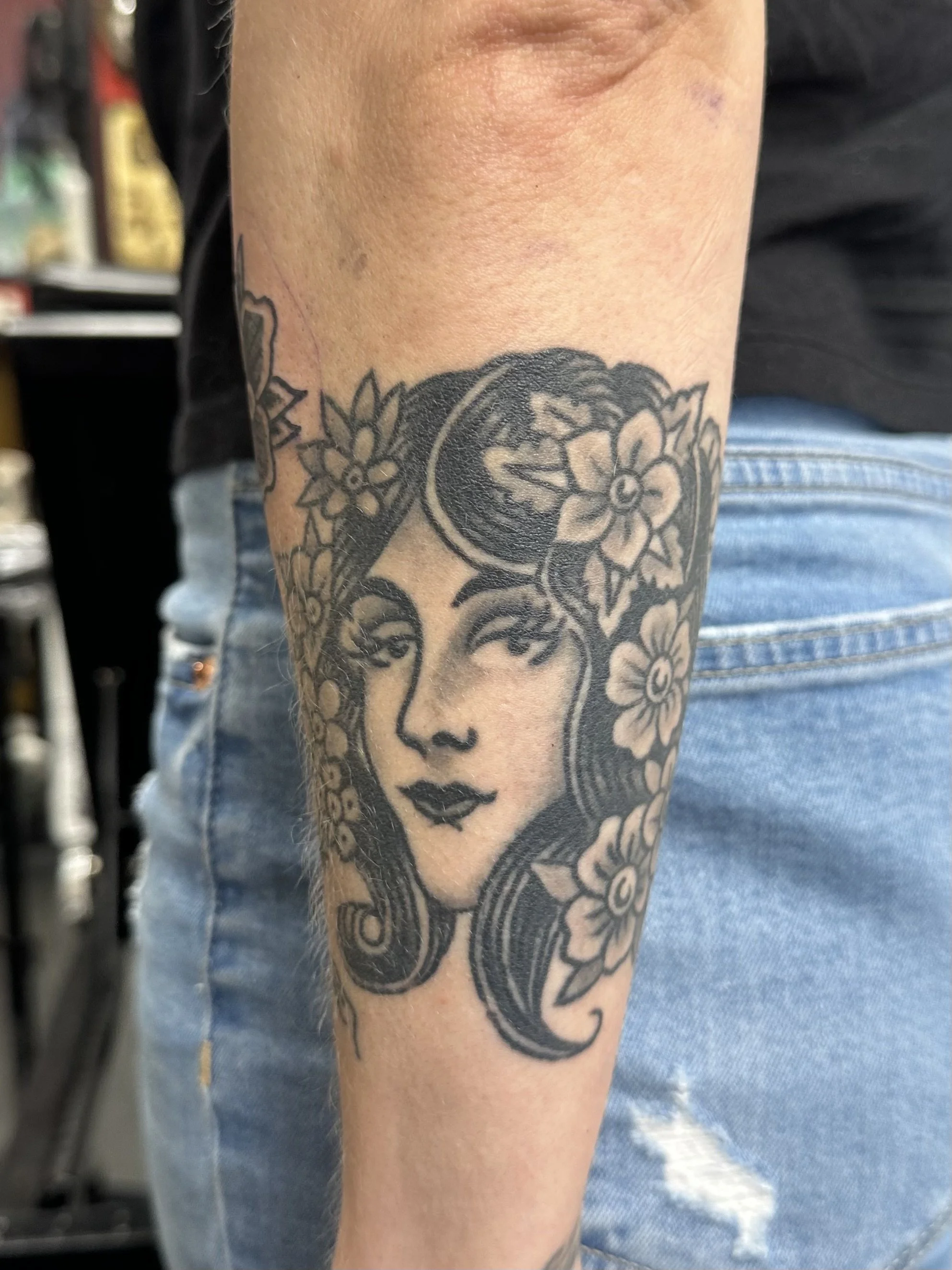 Tattoo of a woman's face surrounded by flowers on a person's arm.