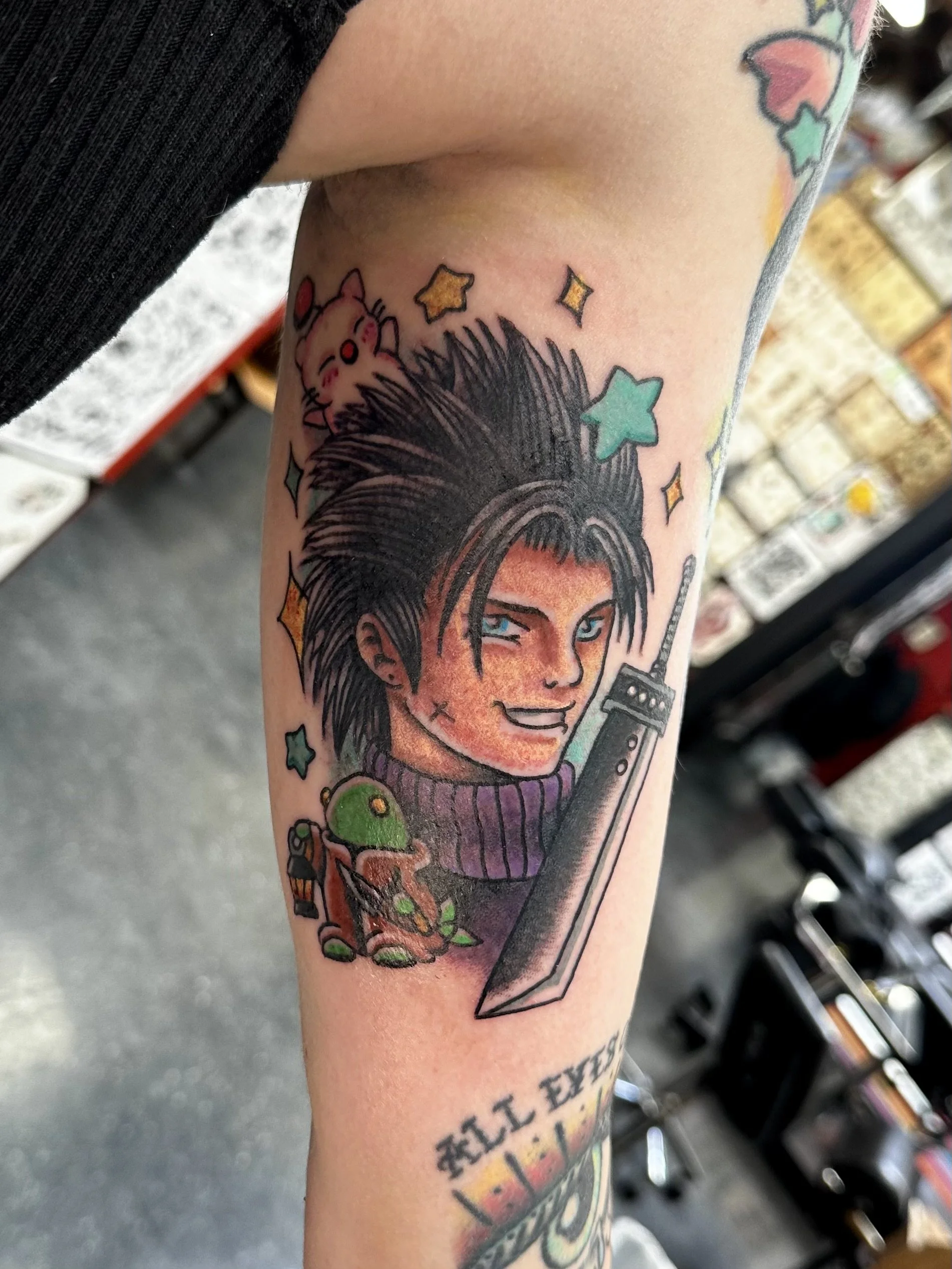 Tattoo of a woman with spiky hair, holding a sword, surrounded by colorful stars and a small pink creature with red cheeks, on an arm.