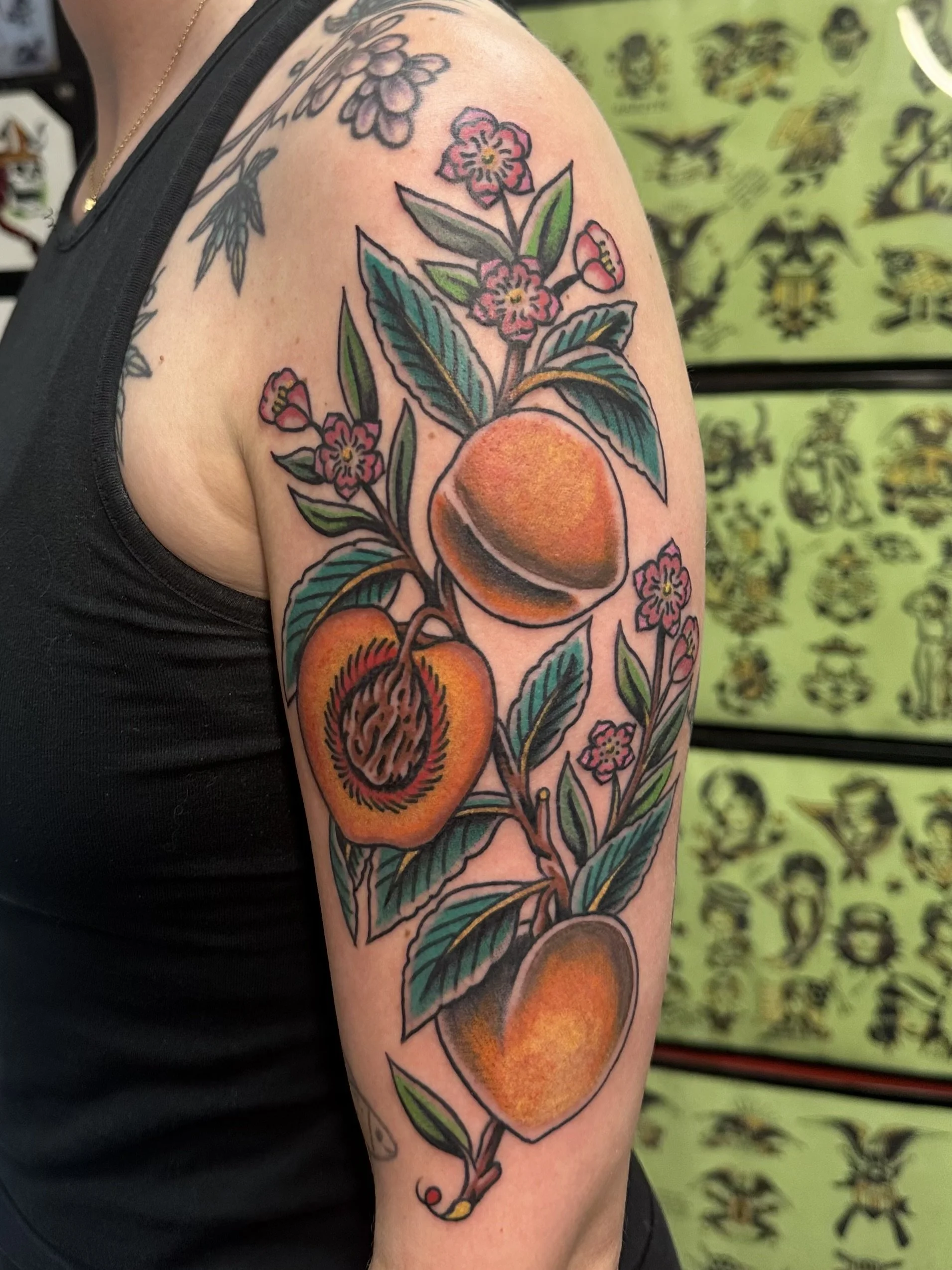 Colorful tattoo of peaches, leaves, and pink flowers on a person's upper arm.