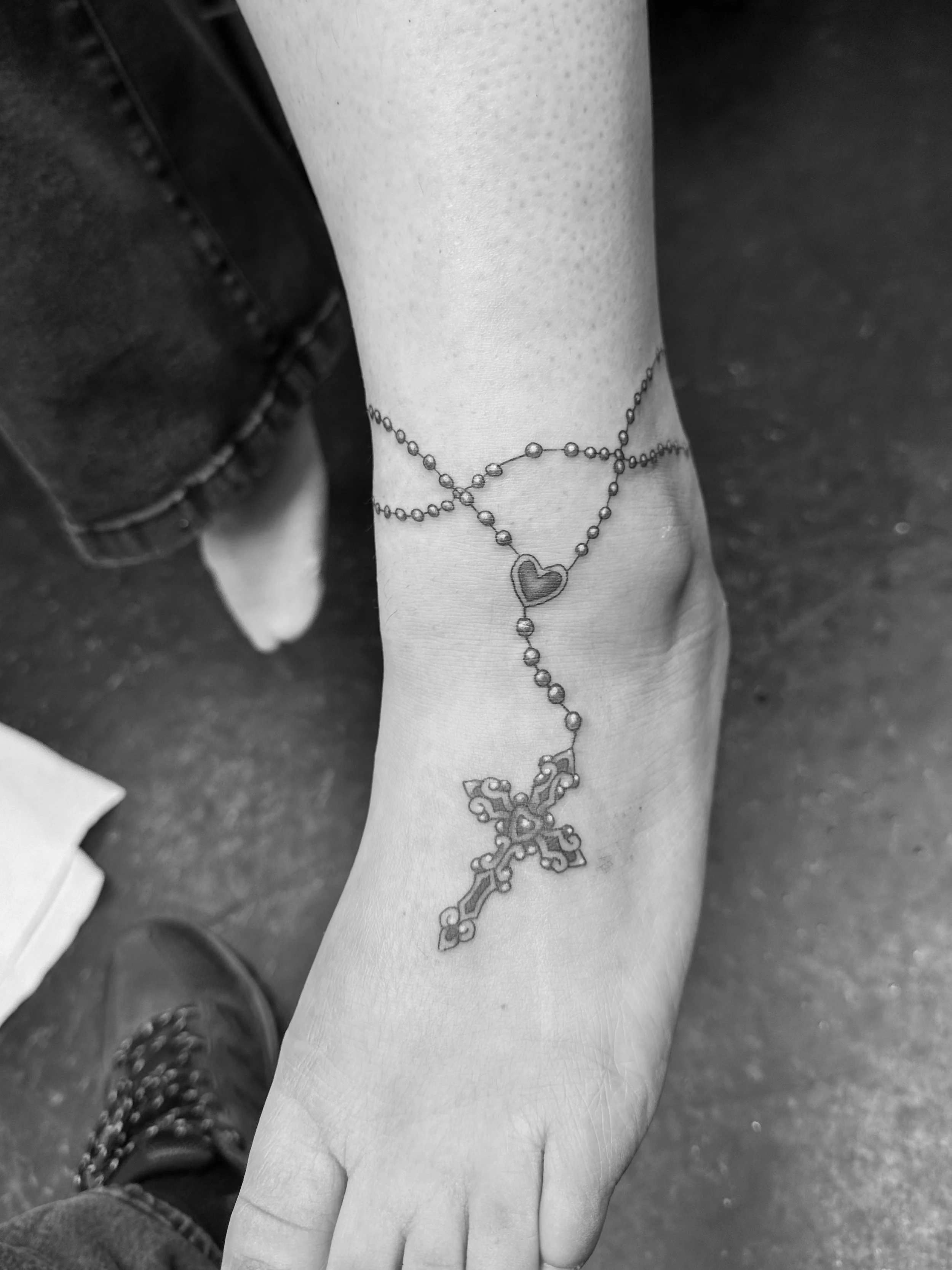 Close-up of a person's wrist and hand with a tattoo of a cross and rosary beads.