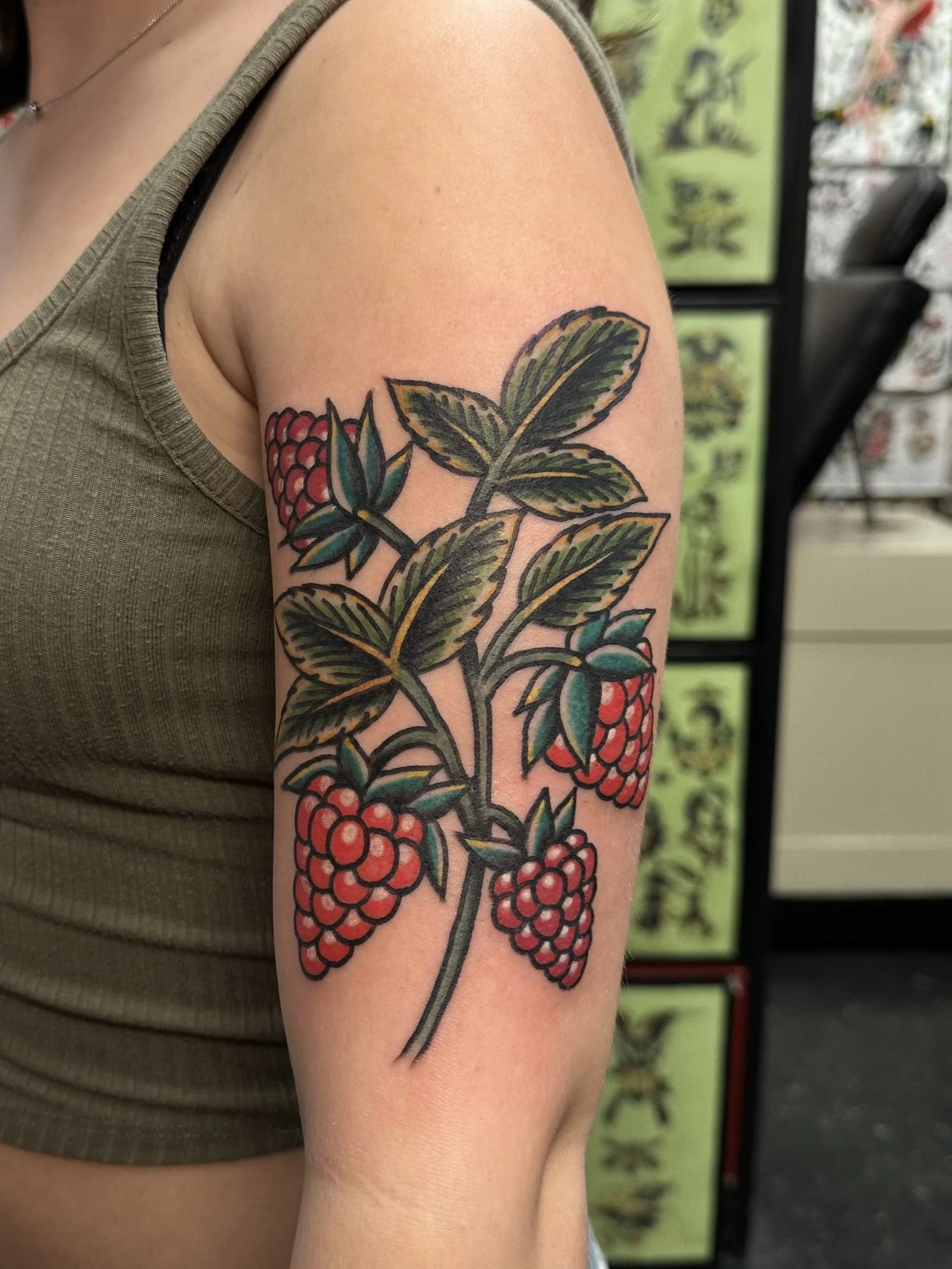 A colorful tattoo of raspberries and green leaves on a person's upper arm.