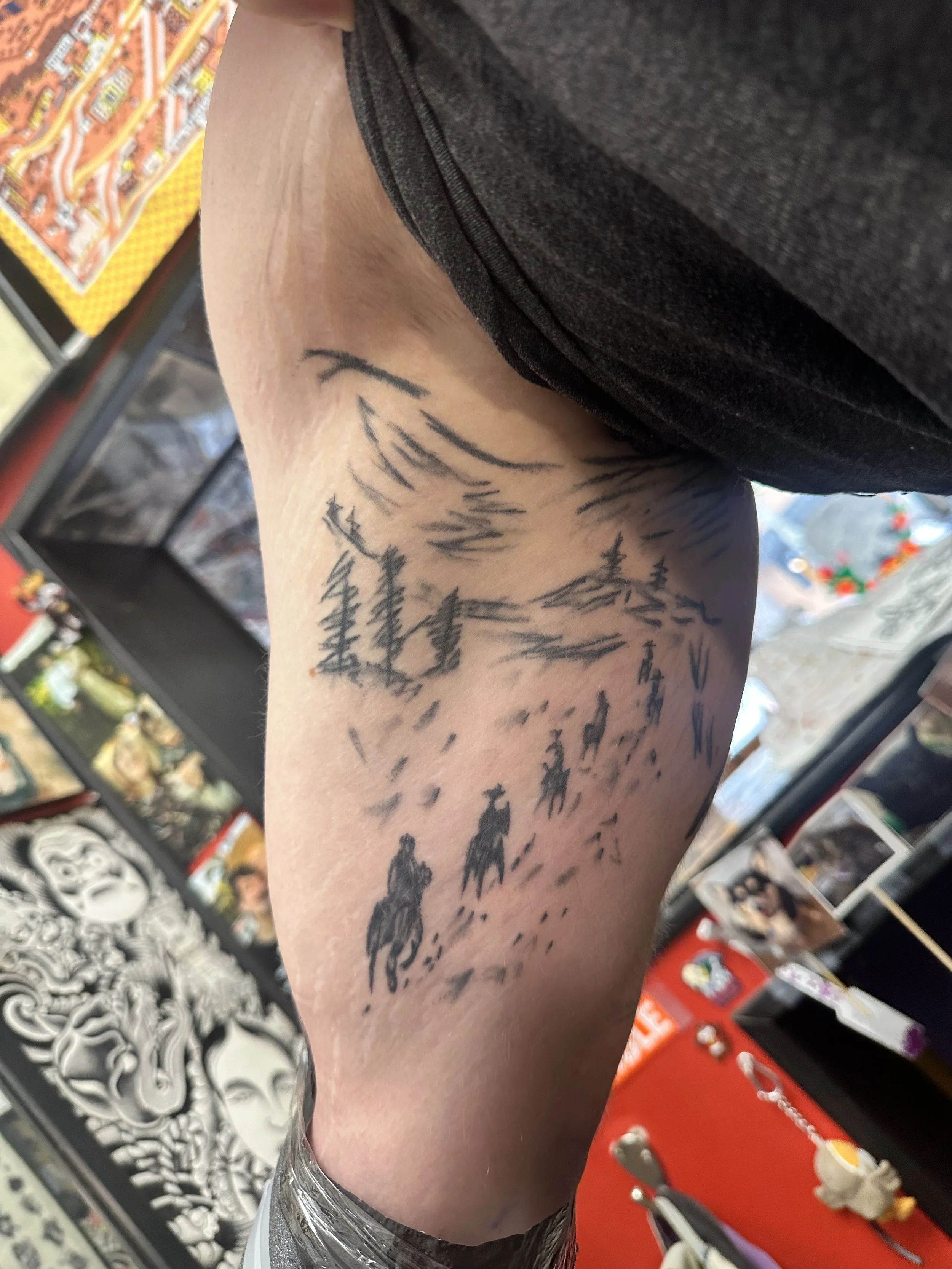 A person's arm with a black ink tattoo of a mountain landscape, including trees and peaks.
