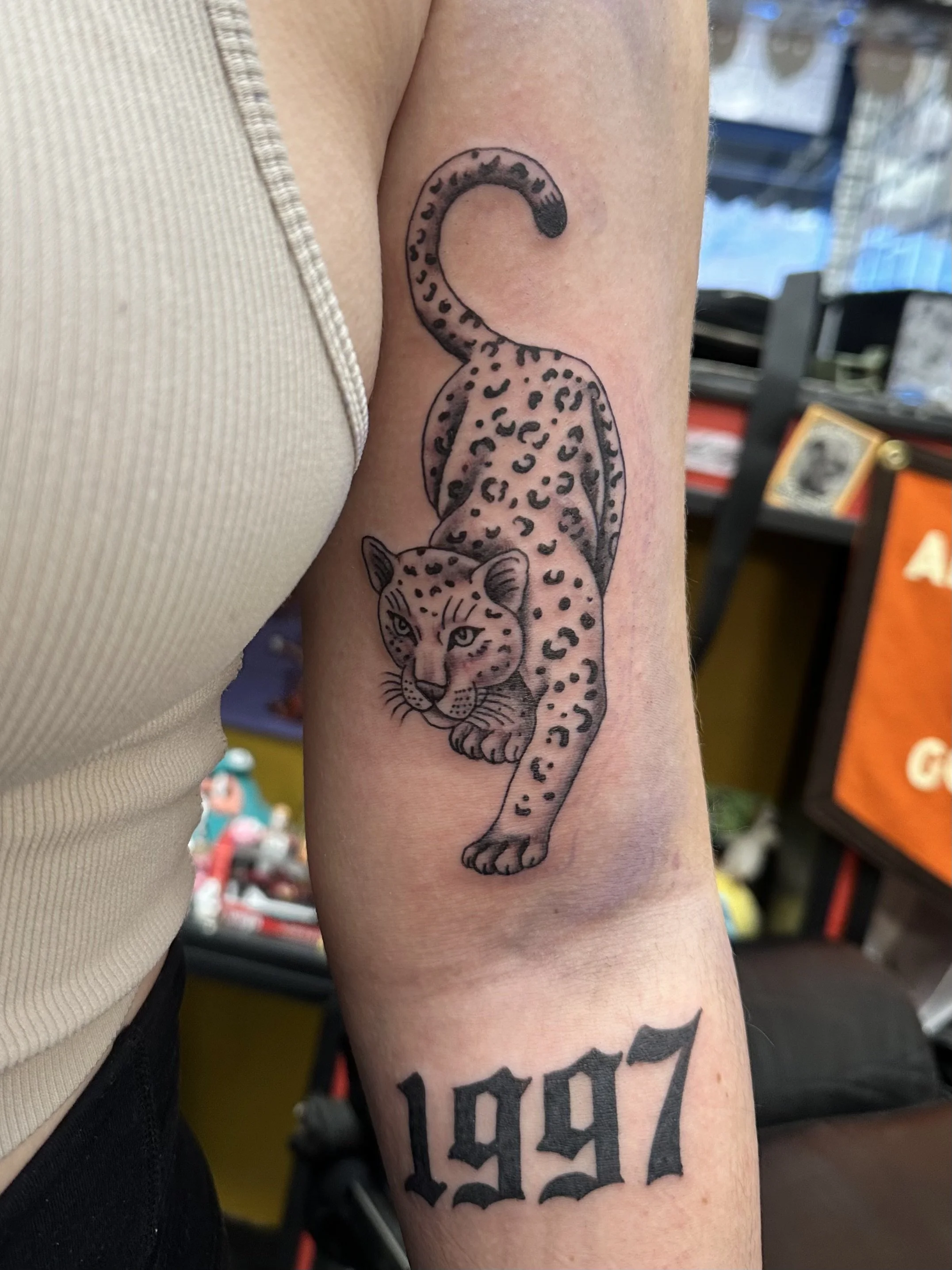 Tattoo of a leaping leopard on person's upper arm, near shoulder.