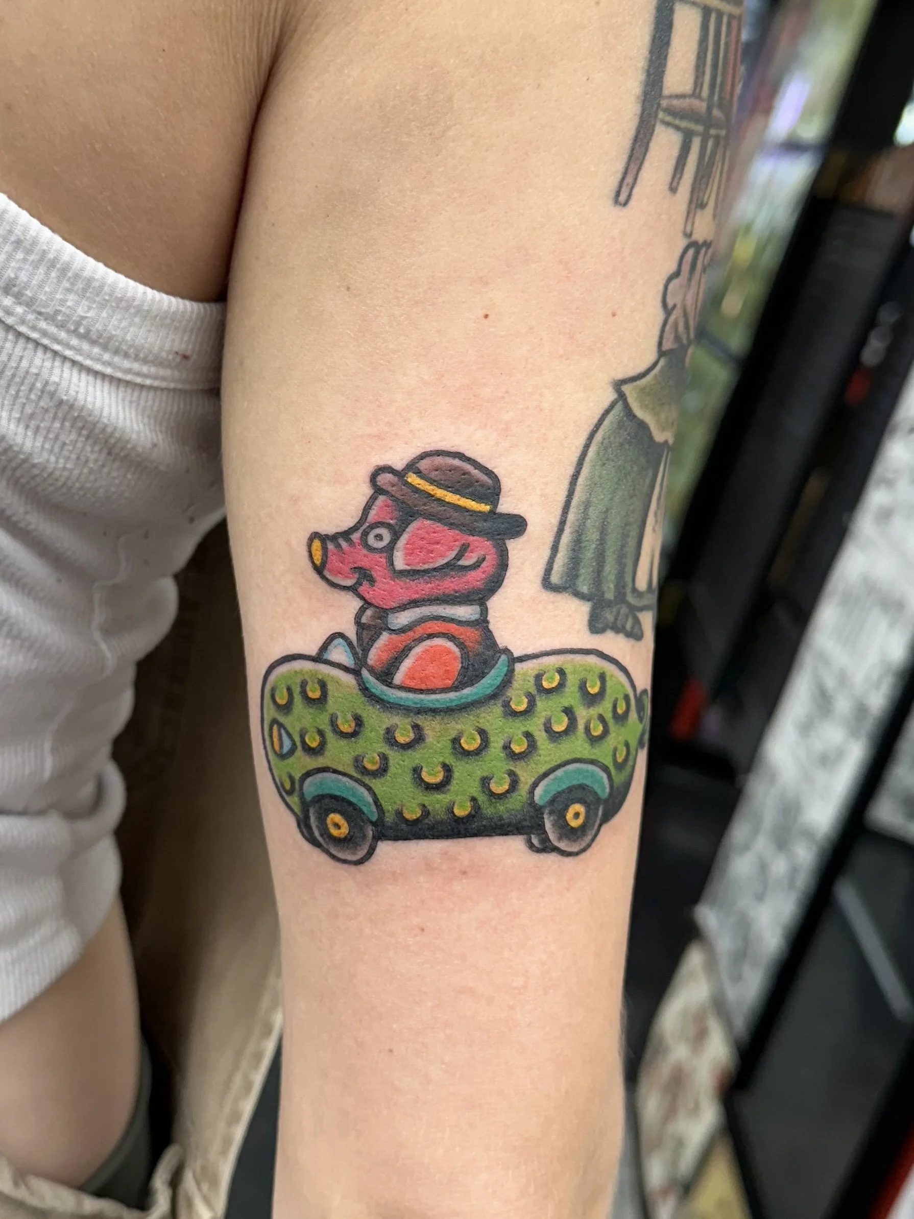 Colorful tattoo of a clown sitting in a green car on upper arm.