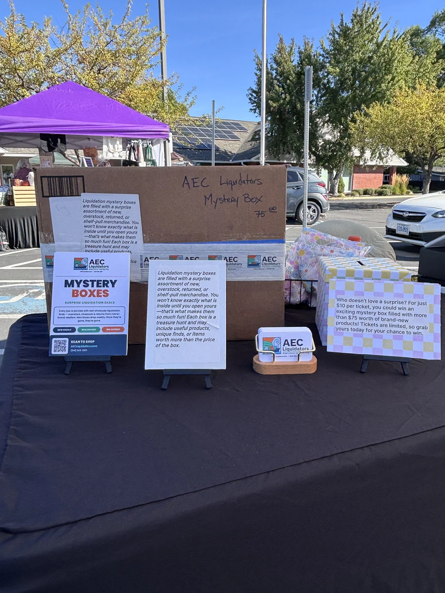 AEC Liquidators Market event we set up a 10X 20 foot tent and sell overstock & mystery boxes by AEC Liquidators. The booth has signs explaining the contents of the mystery boxes, which are surprise liquidation deals filled with various items.