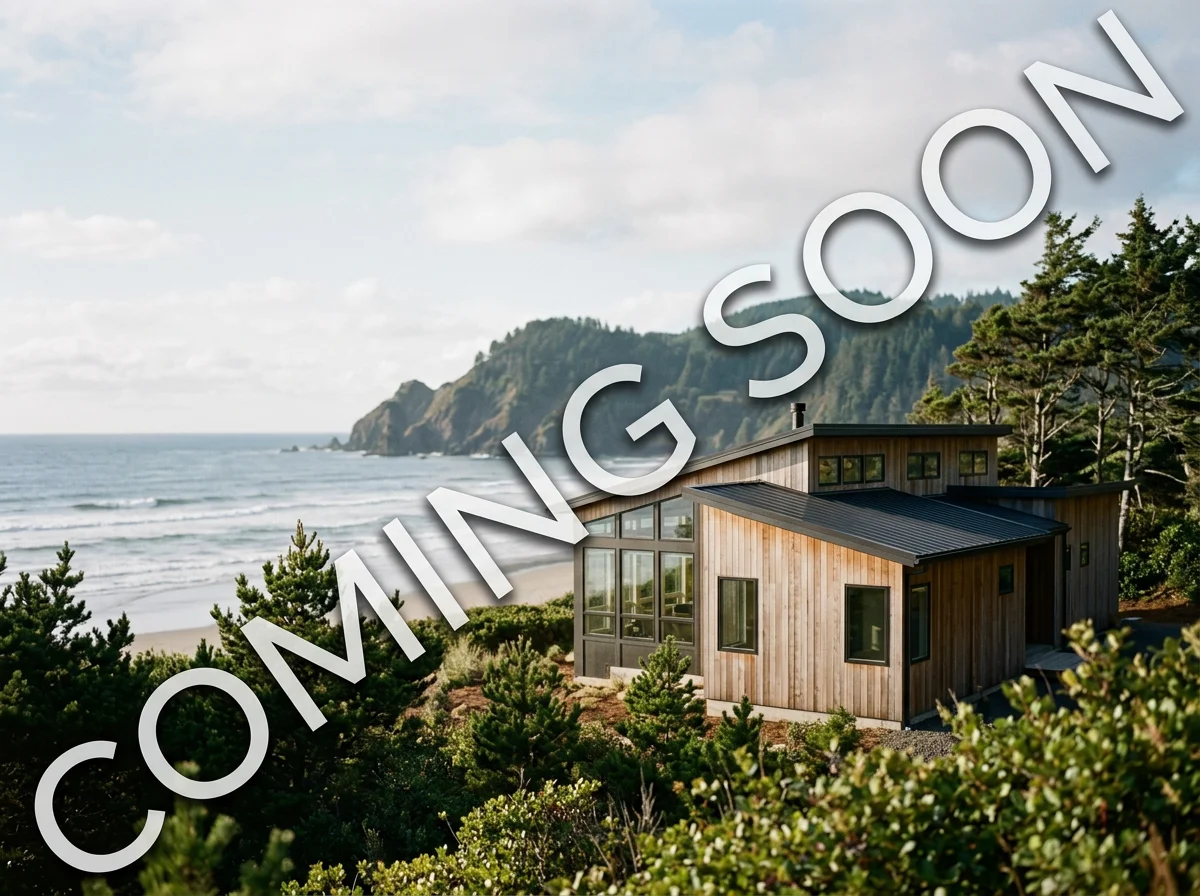Modern wooden house overlooking a beach and ocean with a backdrop of green hills and trees.