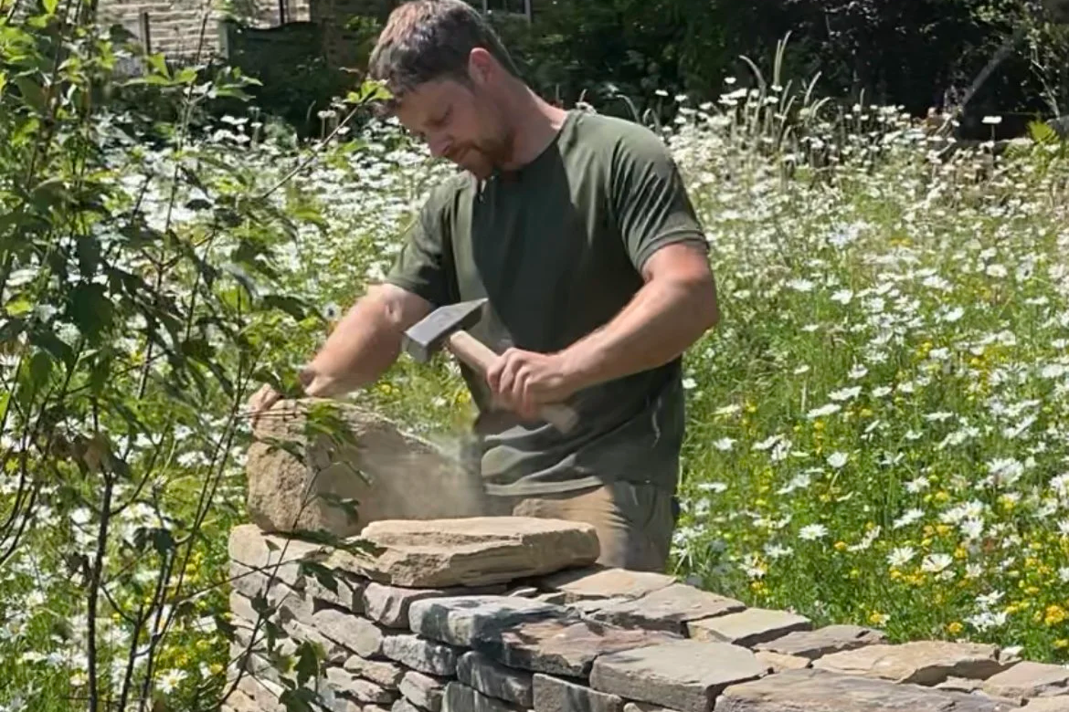 Man building a stone wall outdoors on a sunny day.