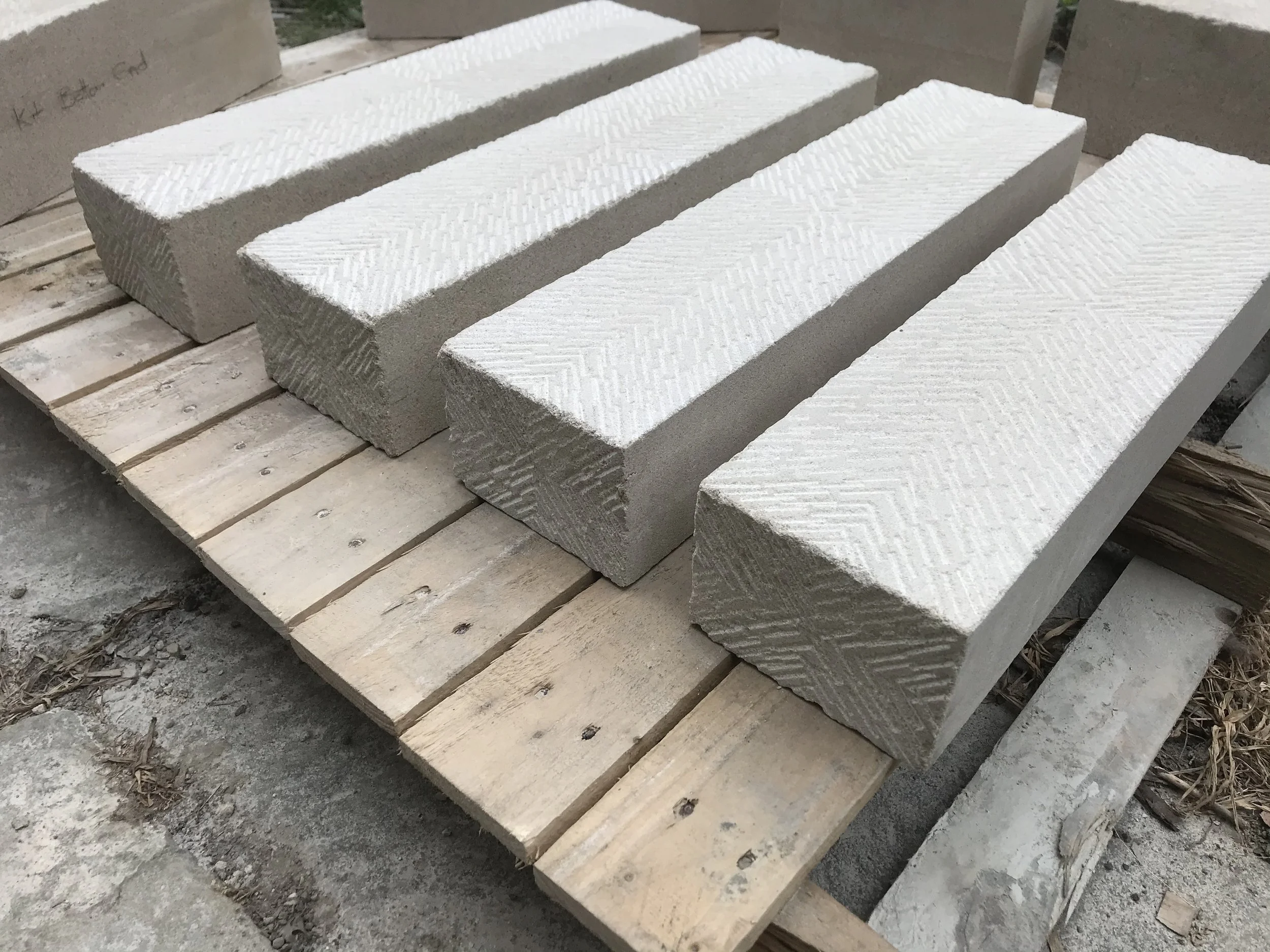 Several large white cement bricks with textured surfaces placed on wooden pallets outdoors.
