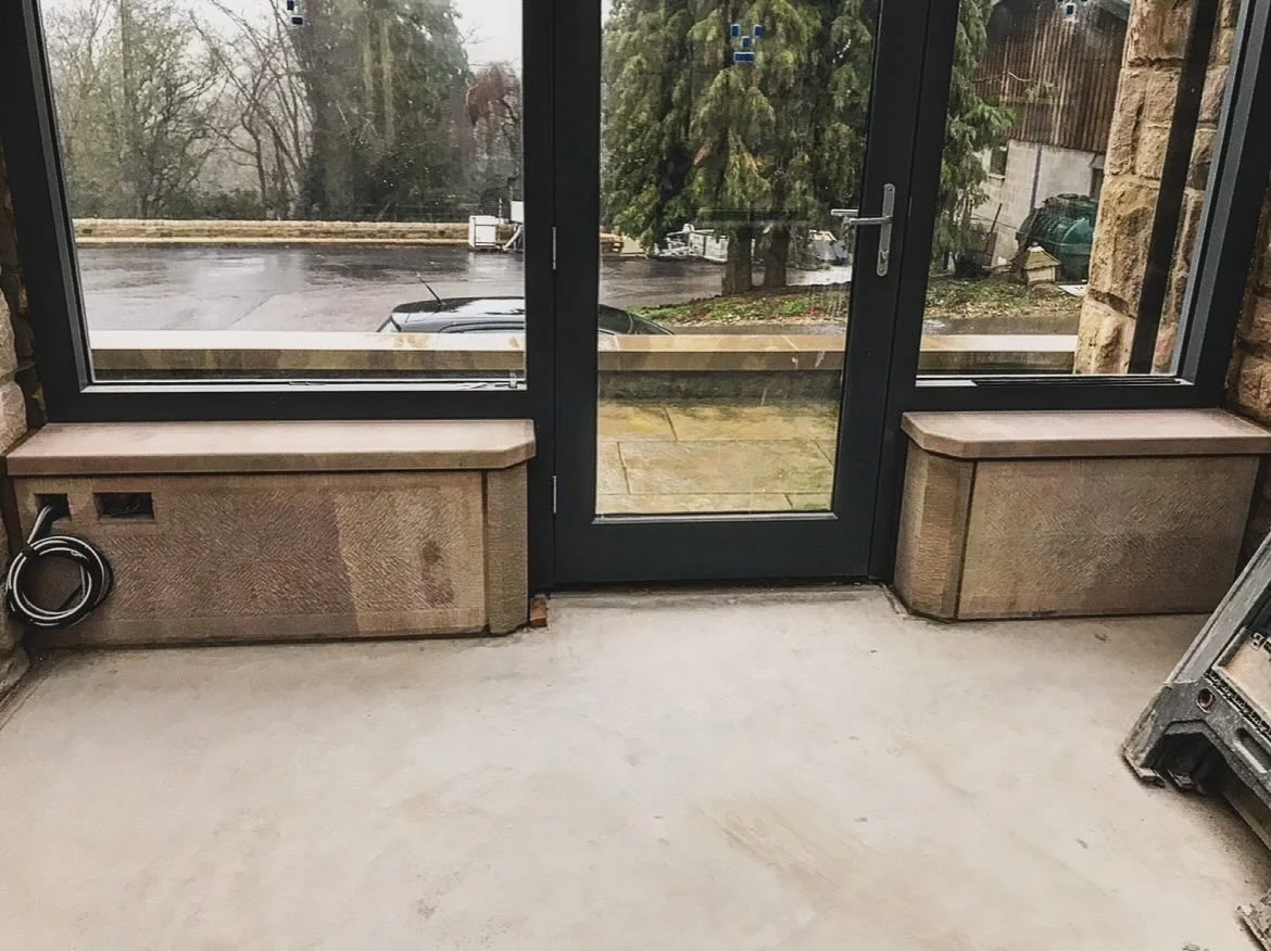 View of an indoor space with concrete floor and large glass door leading to an outdoor parking lot and trees.
