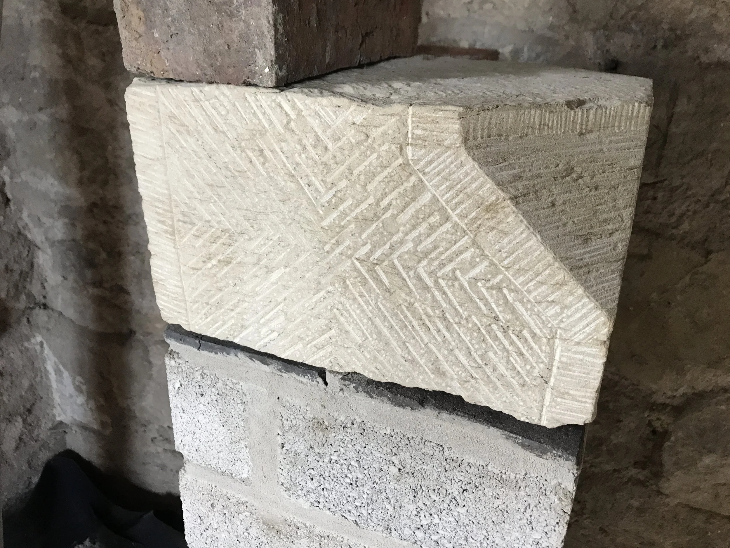 Close-up image of three stacked stone blocks, showcasing detailed carvings and textures, placed against a rough brick wall background.