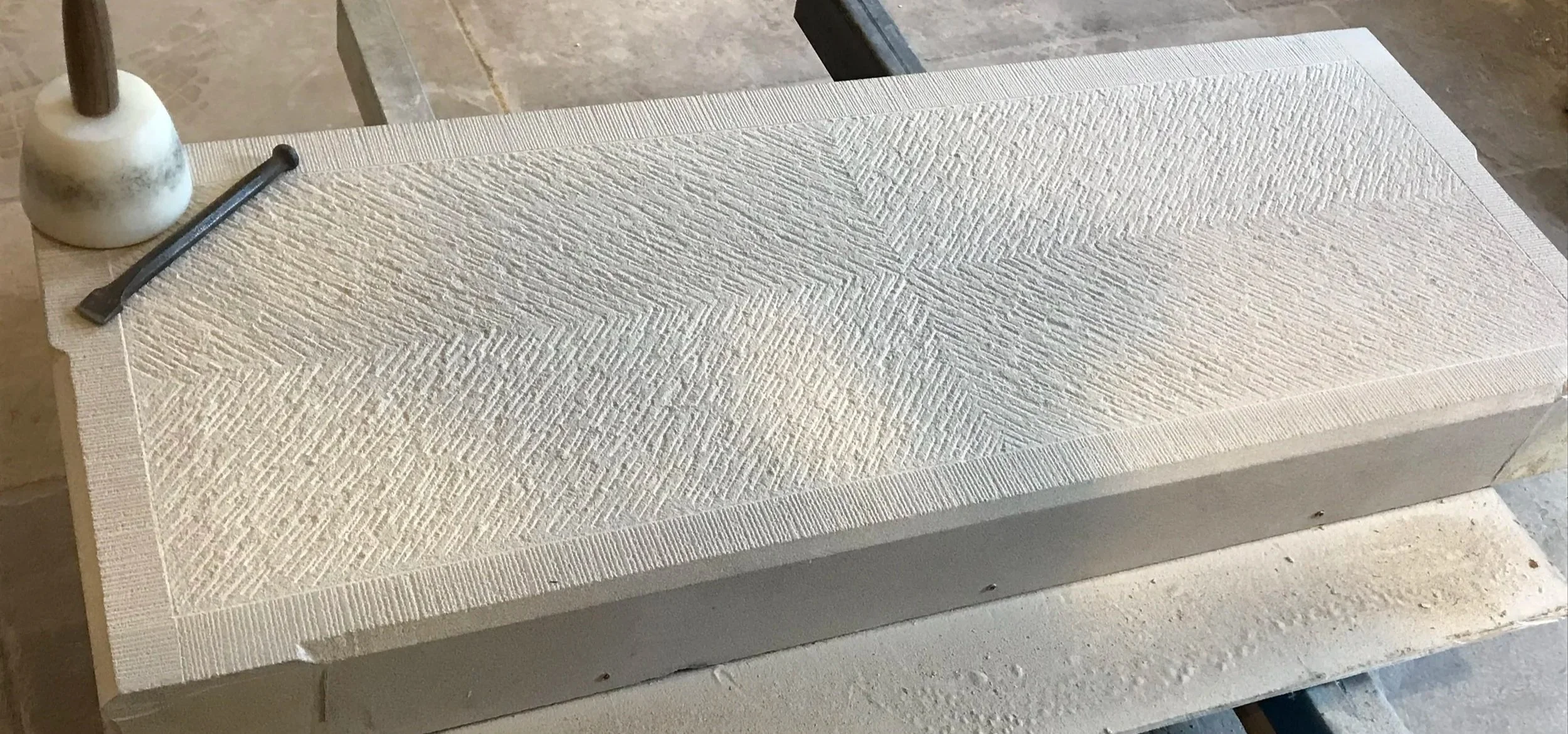A rectangular stone block with textured carved patterns on the top surface, resting on a workbench in a workshop.