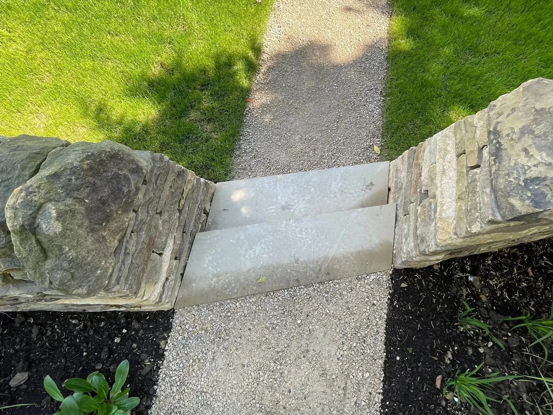 A gravel pathway bordered by a stone wall and green plants, with grass on either side.