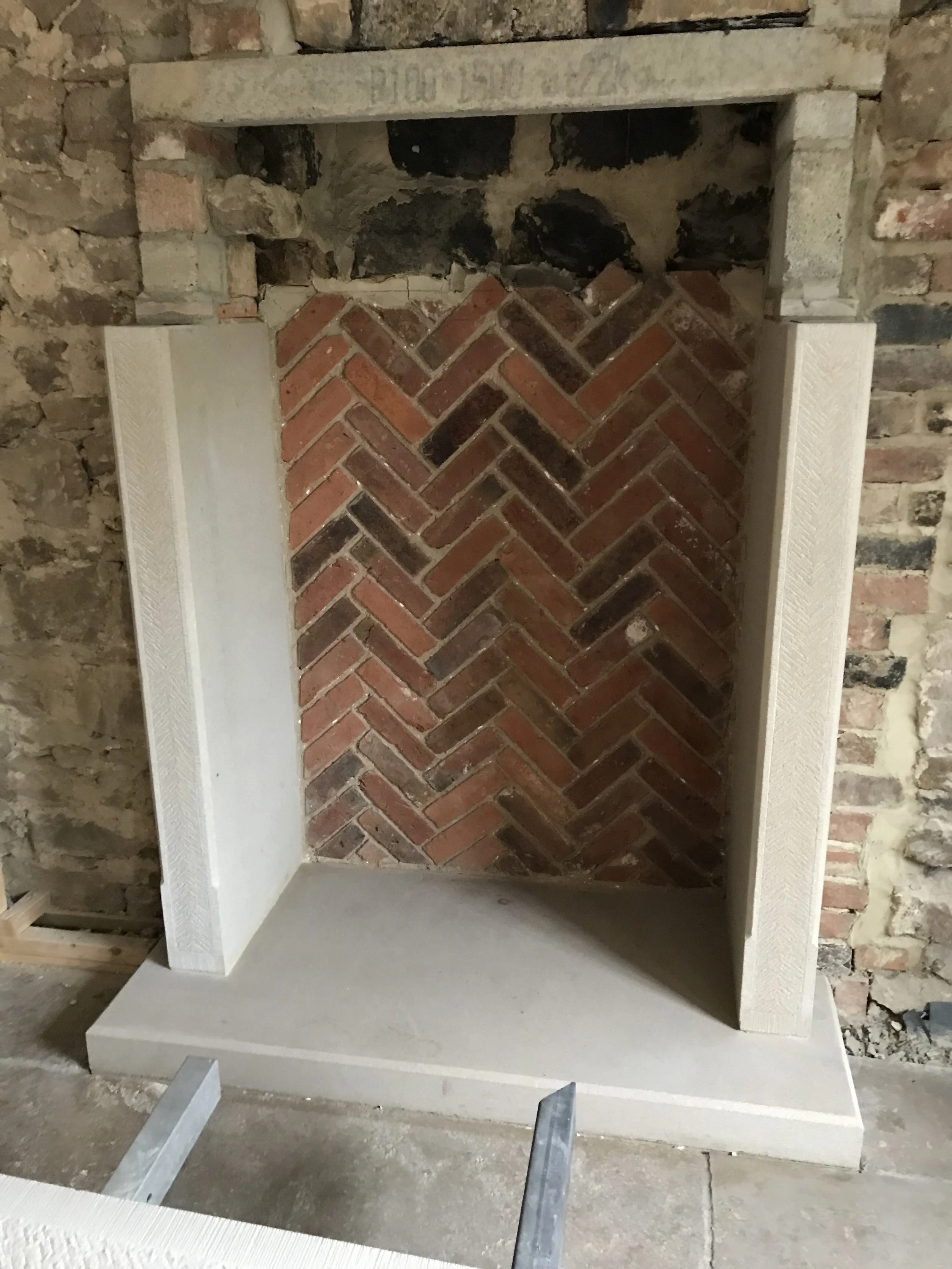 A fireplace with a brick interior, framed by a white mantelpiece, in an unfinished brick wall.