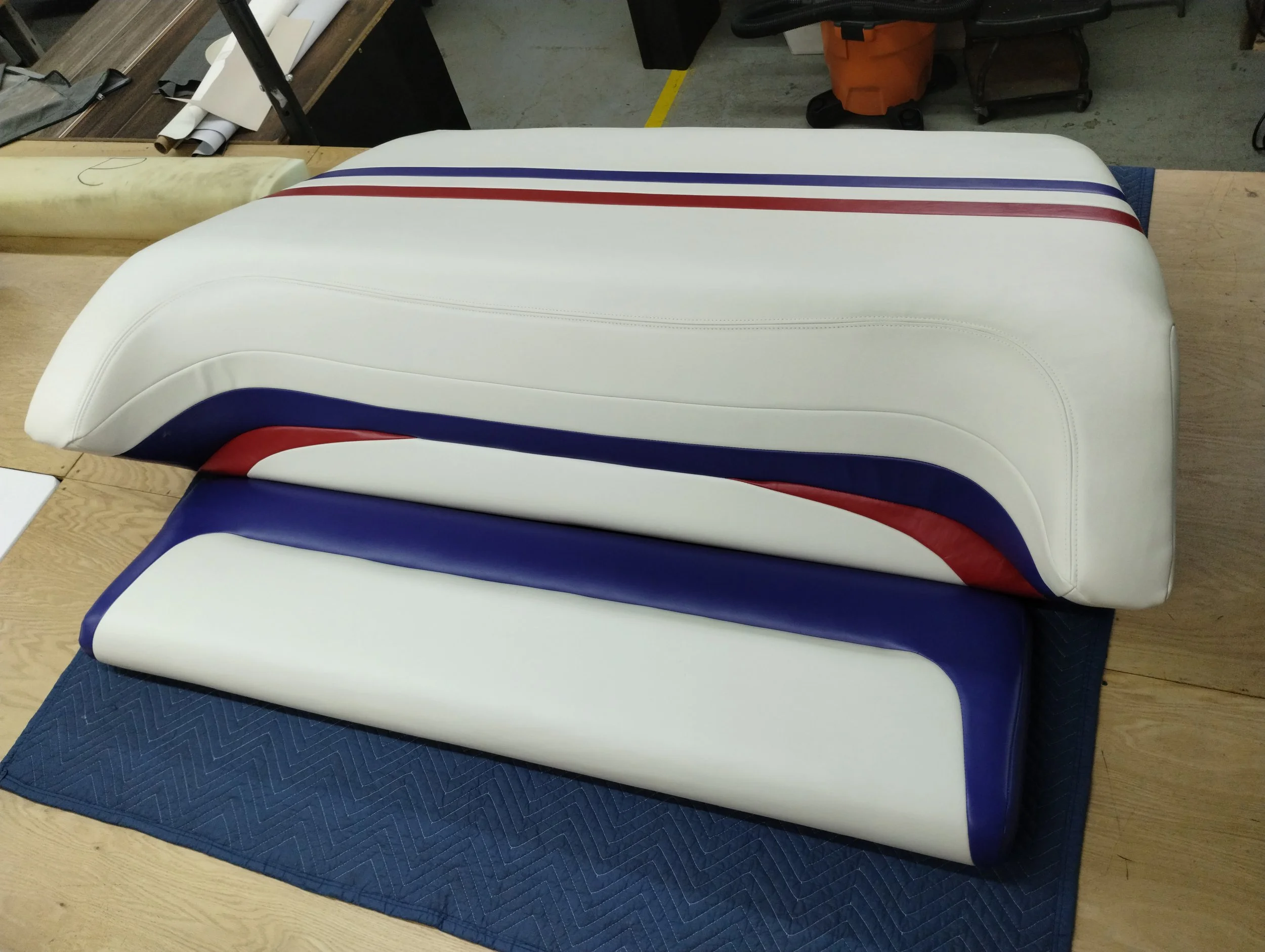 Multiple white, red, and blue cushioned seats arranged on a wooden table in a workshop setting.