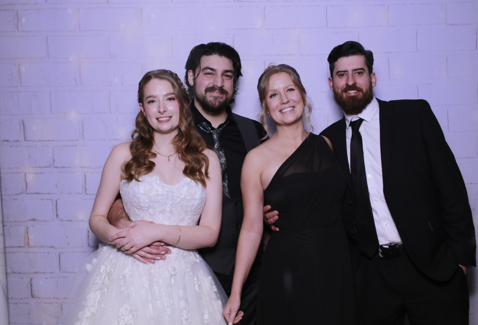 Group of four people at an event smiling against a white brick wall. Two women and two men dressed in formal attire.