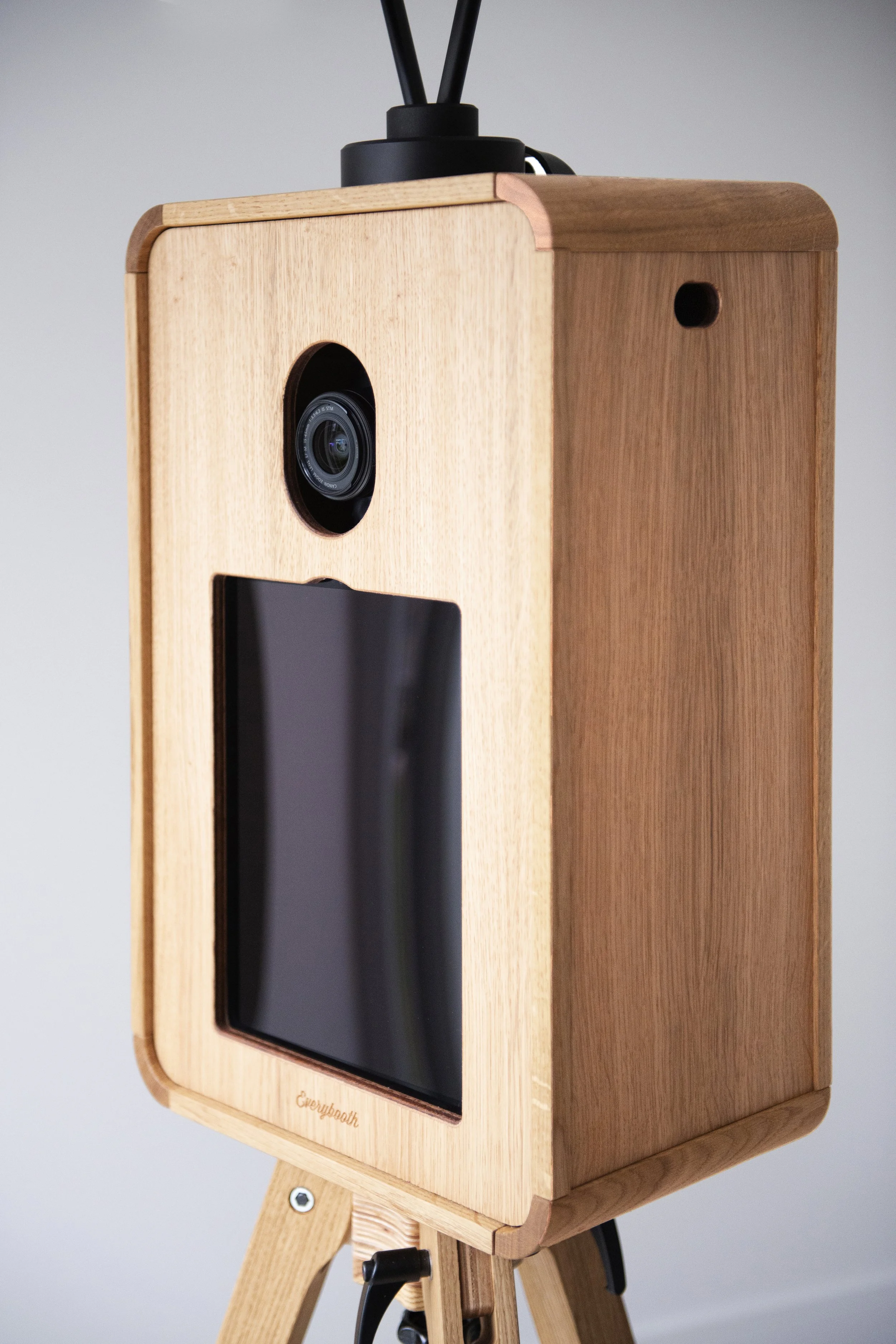 A wooden device mounted on a tripod with a camera lens and a digital screen, possibly a 3D scanner or photogrammetry station.
