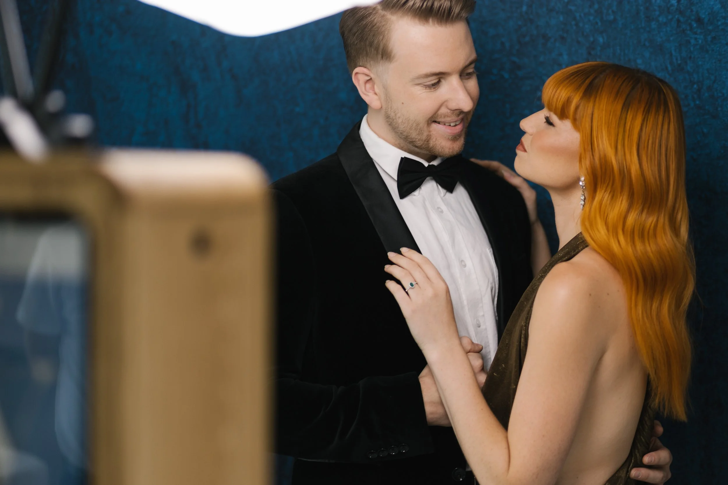Man in tuxedo and woman with red hair in an embrace, looking at each other affectionately.