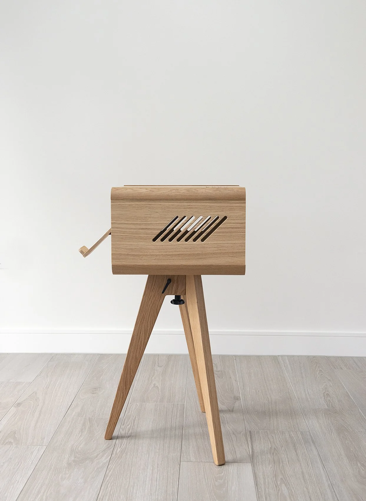 A wooden object on a tripod stand with a slatted front panel and a crank on the side, against a white background.