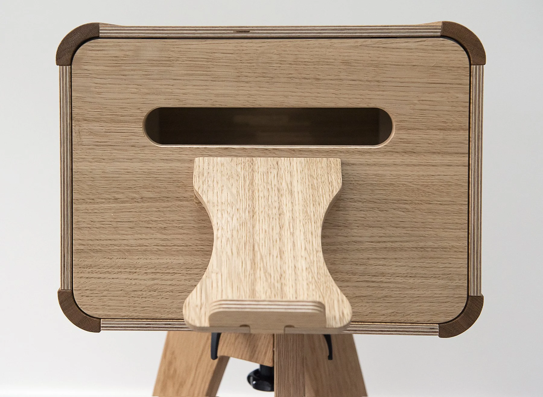 Close-up view of a wooden table with a small, curved cut-out tray in the center, supported by a tripod stand, against a plain light background.