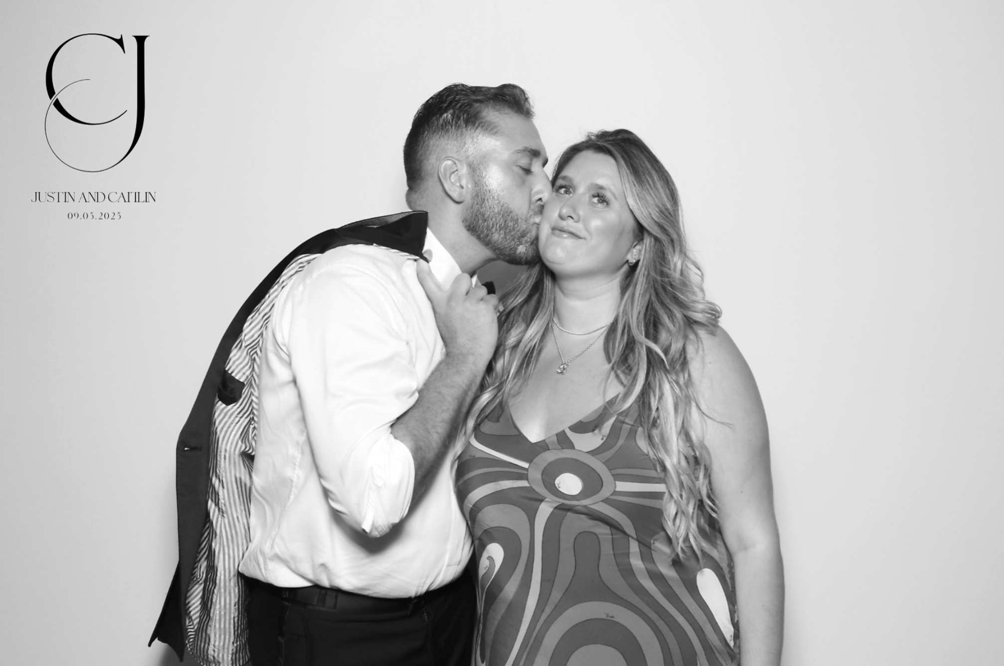 Black and white photo of a couple, a man kissing a woman on the cheek, both smiling, against a plain background with initials and names in the upper left corner, indicating a wedding date of September 5, 2025.
