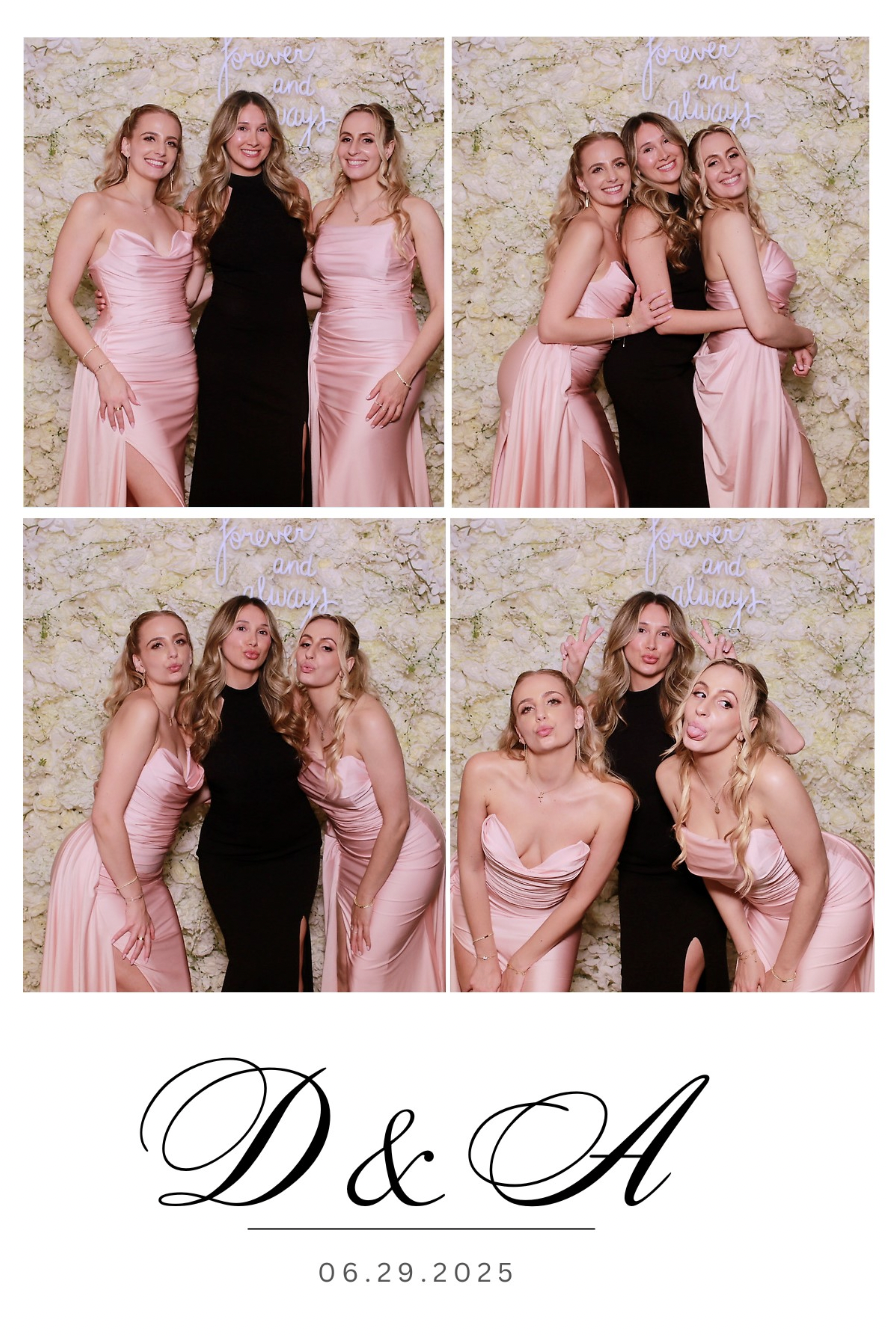 Four women posing in a photo booth at a celebration. The women are dressed in pink and black formal gowns, standing in front of a textured wall with a neon sign that says 'forever and always.' The bottom of the image features the initials 'D & A' and