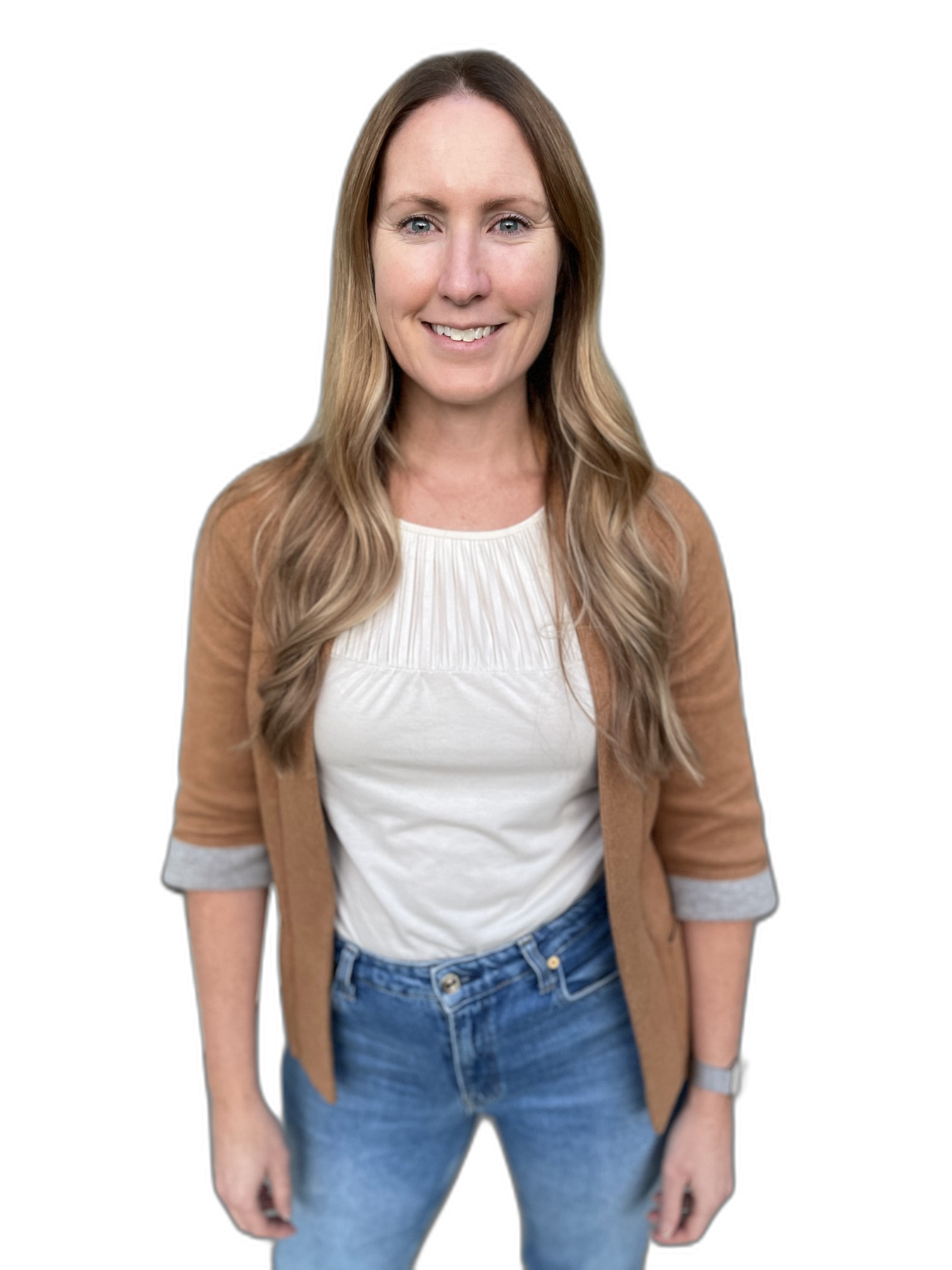 A woman with long, wavy blonde hair wearing a white top, a tan cardigan, and blue jeans standing against a black background.