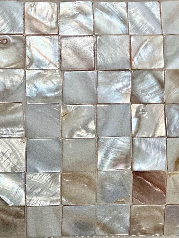 Close-up of a mosaic tiled wall with rectangular and square tiles made of mother of pearl, exhibiting iridescent and reflective surfaces.